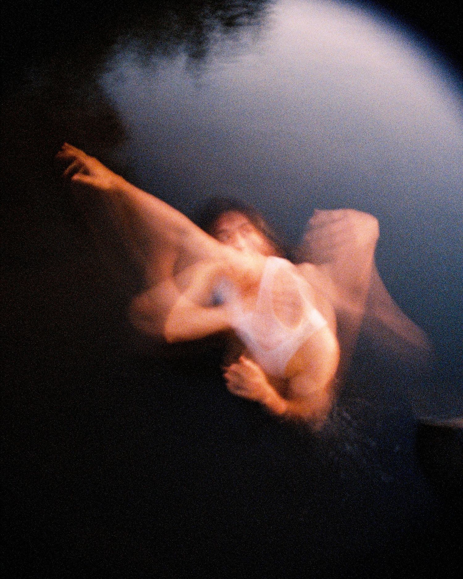 Motion-blurred figure captured mid-movement against dark background with dramatic lighting and ethereal effect.