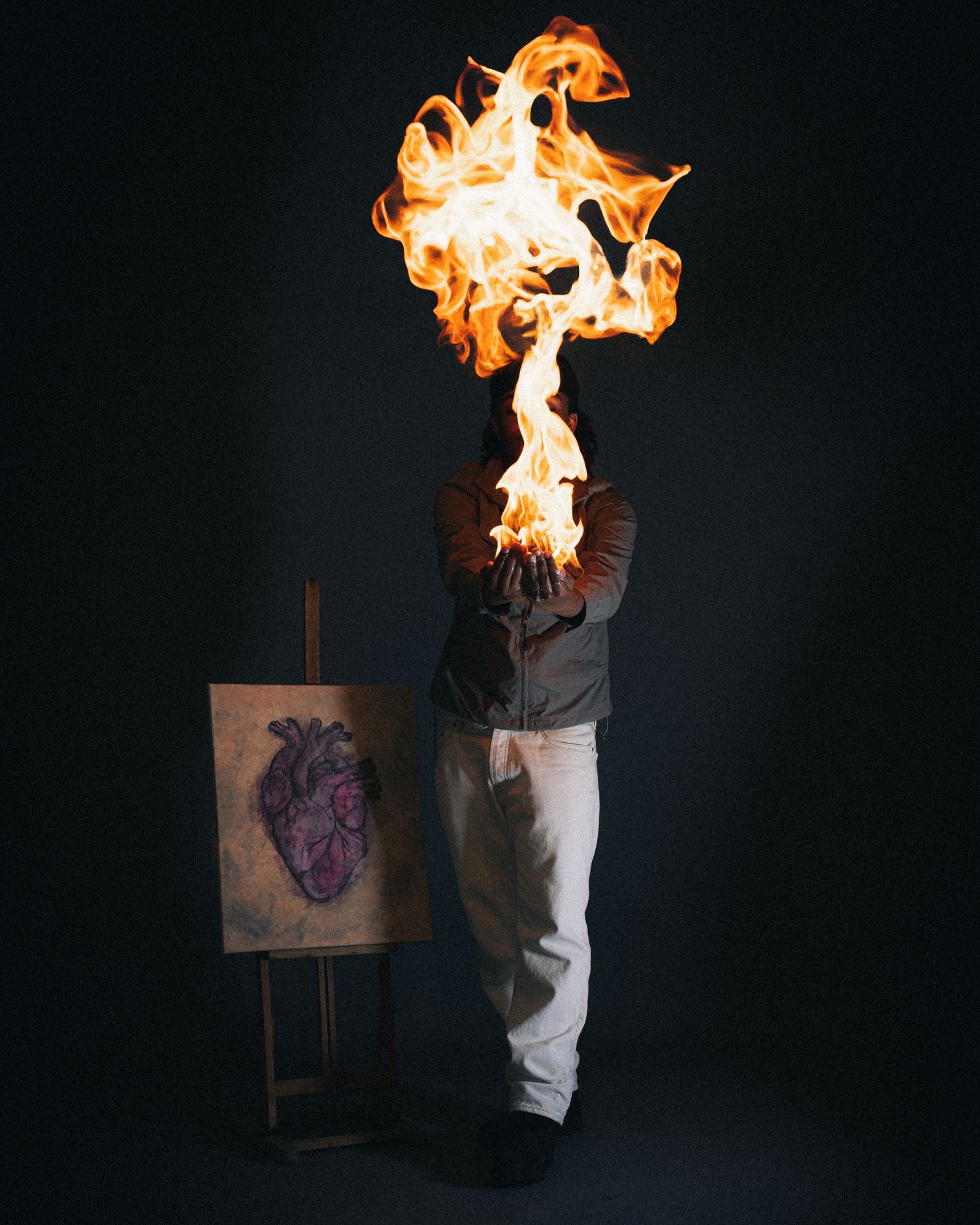 Artistic conceptual photograph showing a figure with flames emanating from top against dark background with anatomical heart sketch.