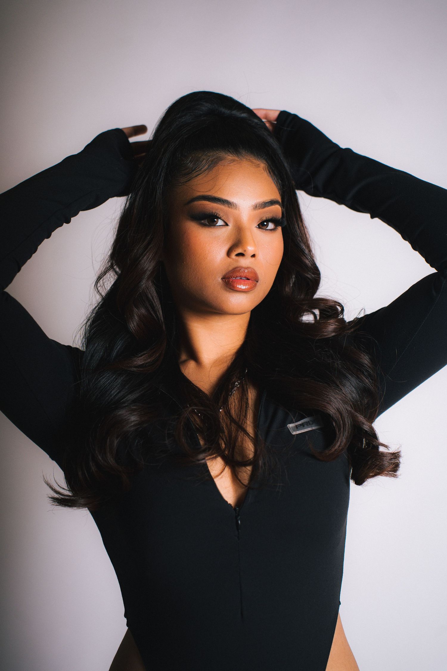 A woman in a black long-sleeve top poses with flowing dark hair against a white backdrop in a glamour photo.