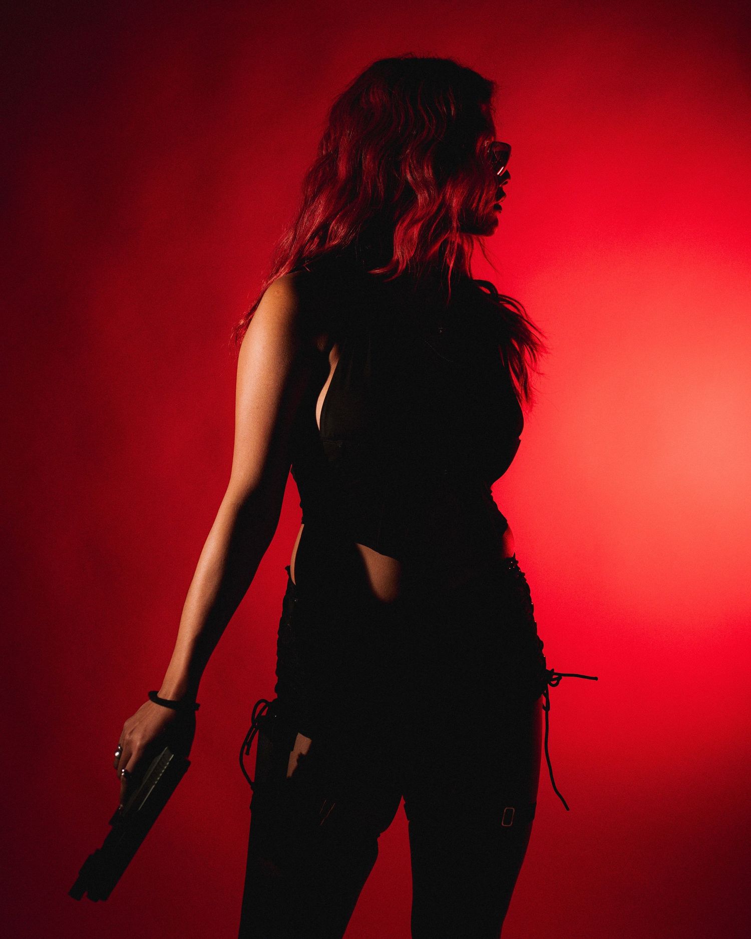 Silhouette figure in dark clothing stands against dramatic red background lighting in moody portrait composition.