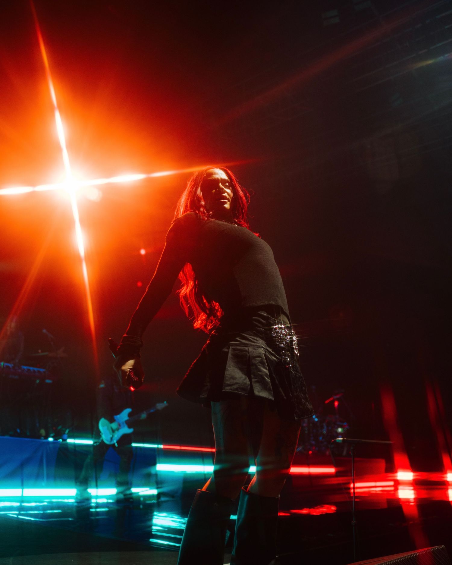 A performer silhouetted on stage with dramatic red lighting and glowing cross effect in the background.