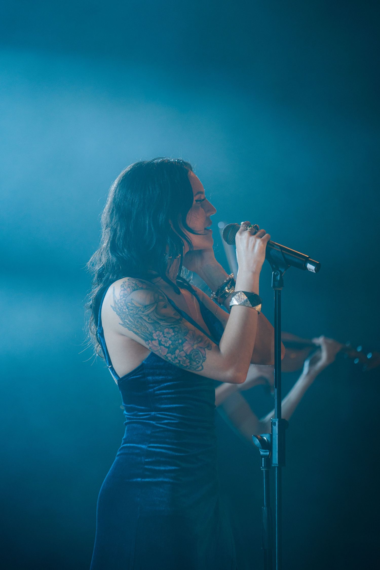 Singer performing on stage in a black dress against atmospheric blue lighting.