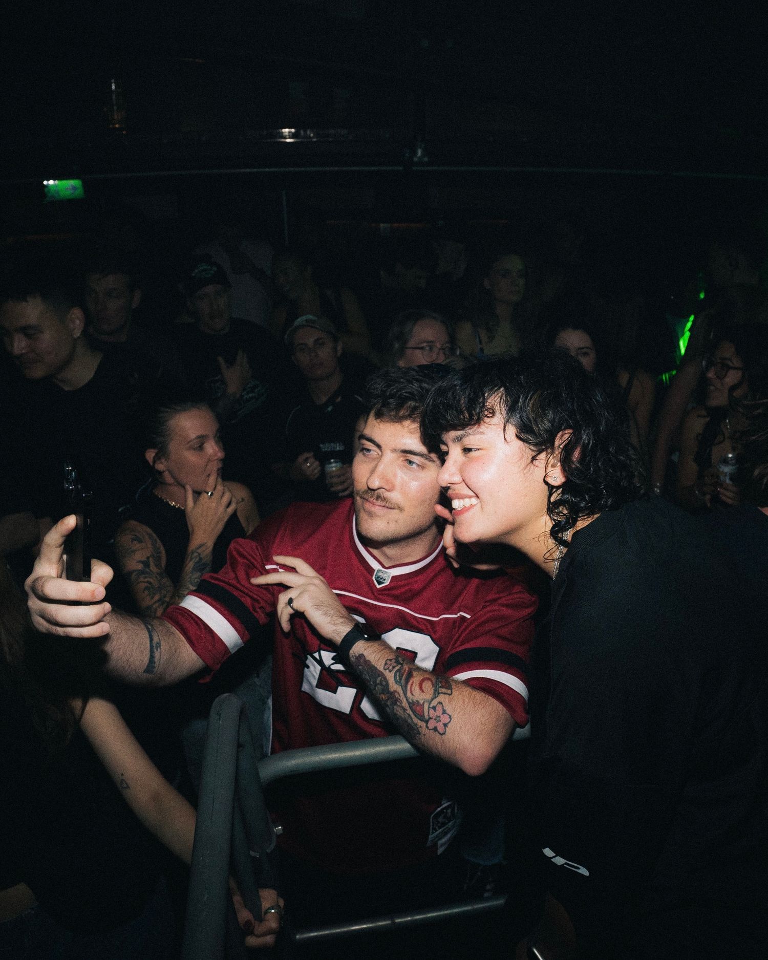 Crowd enjoying music and dancing at dimly lit nightclub venue.