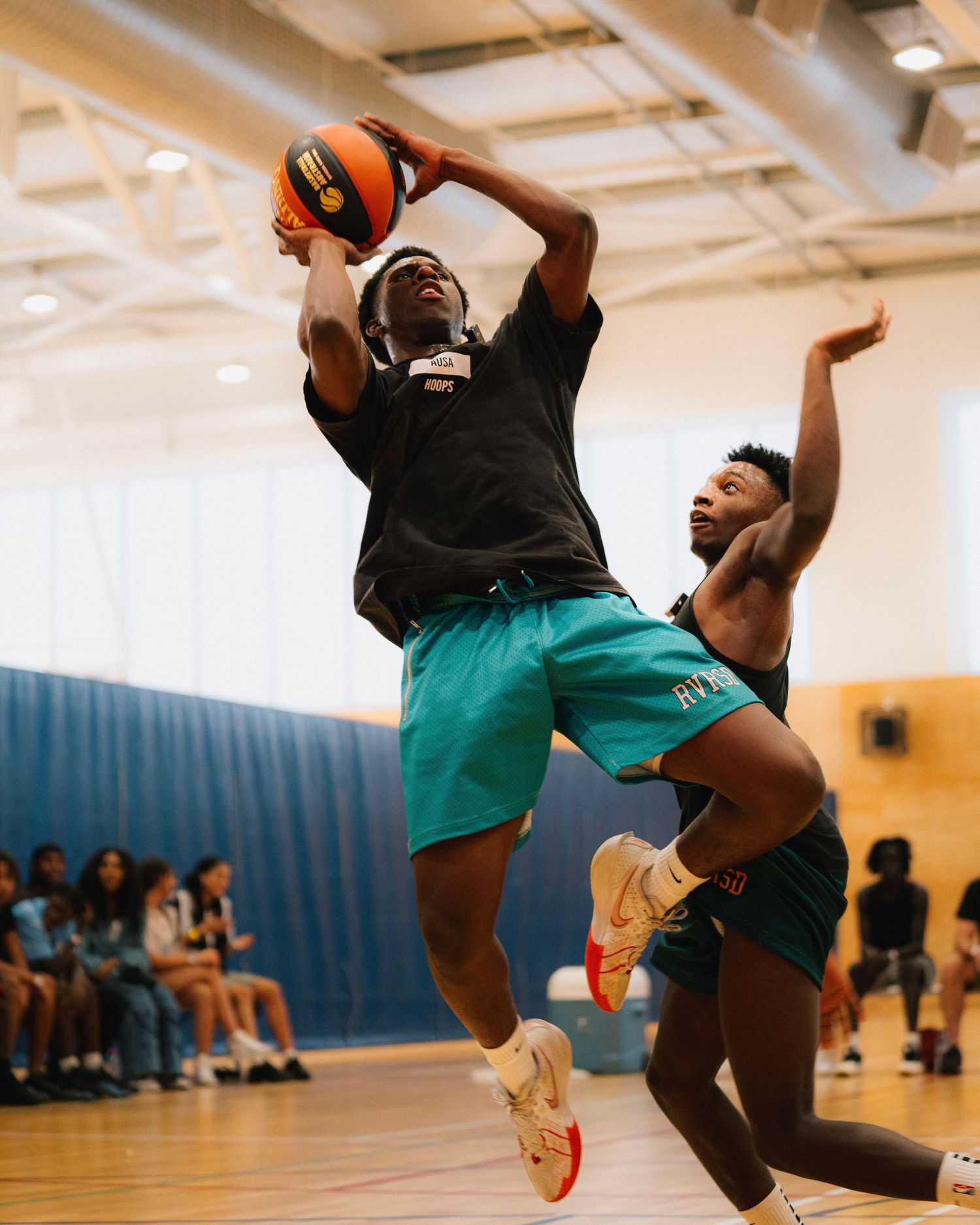 Players in teal shorts competing for a rebound during an indoor basketball game.