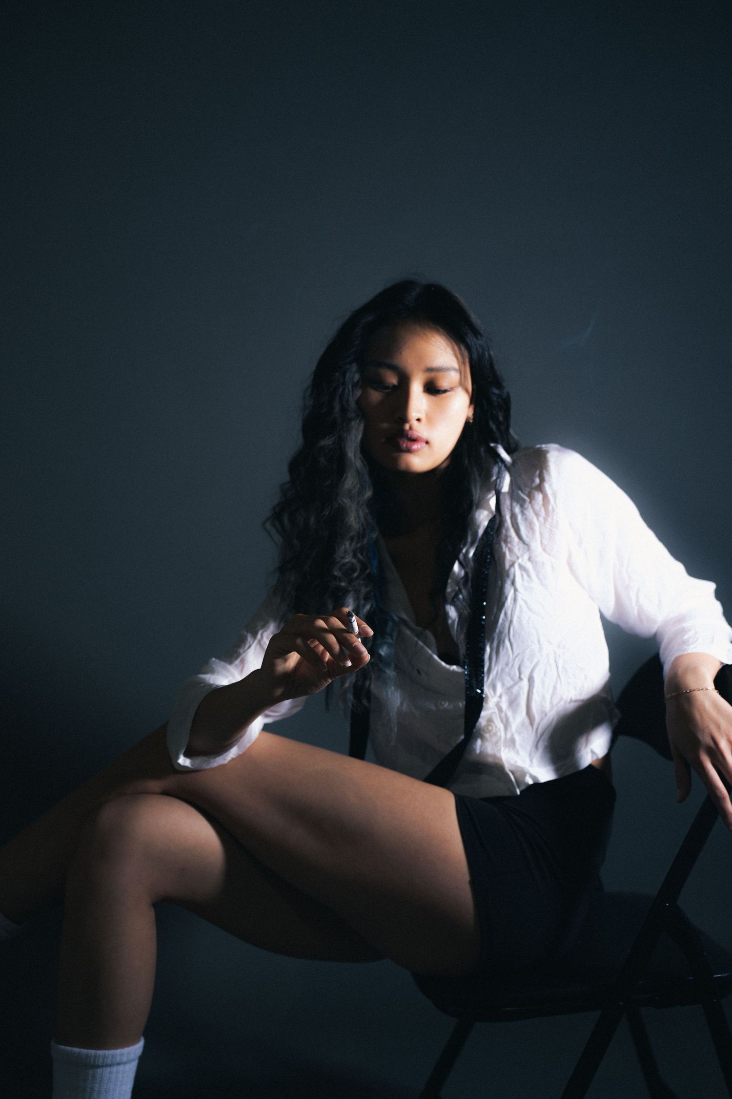 Artistic moody black and white photo series showing someone in white shirt sitting and posing against dark backdrop.