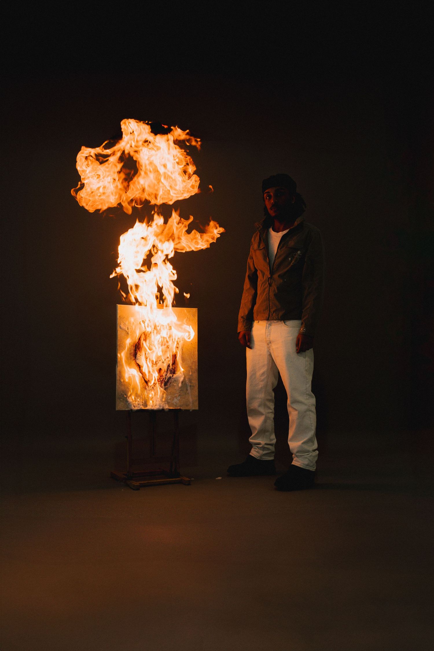 Fire burns from a black box in a dark room as a person stands nearby observing the dramatic flames.