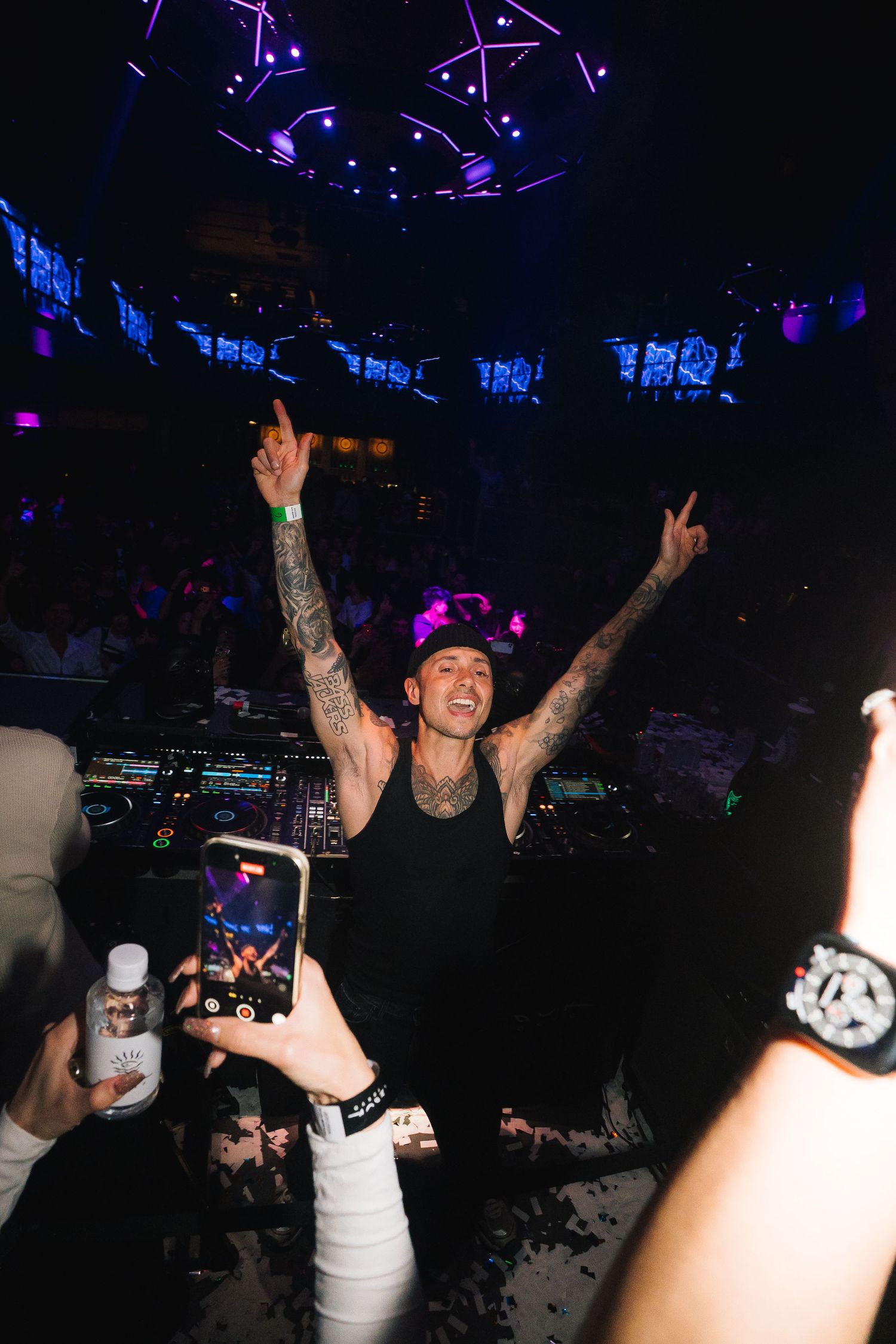 DJ Marshmello performs at a nightclub with blue and purple lighting while fans record with their phones.