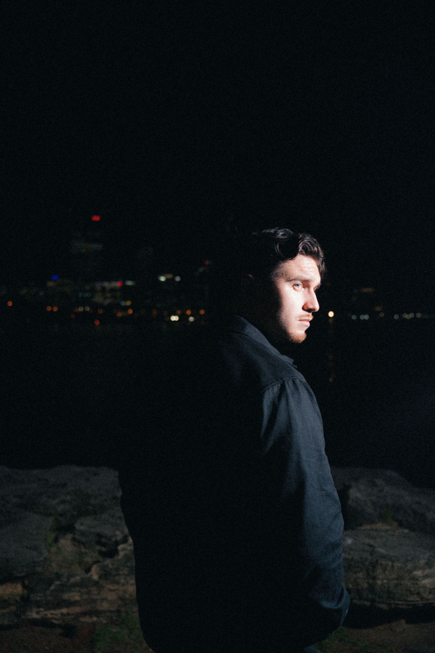 Moody nighttime profile shot with city lights twinkling in background.