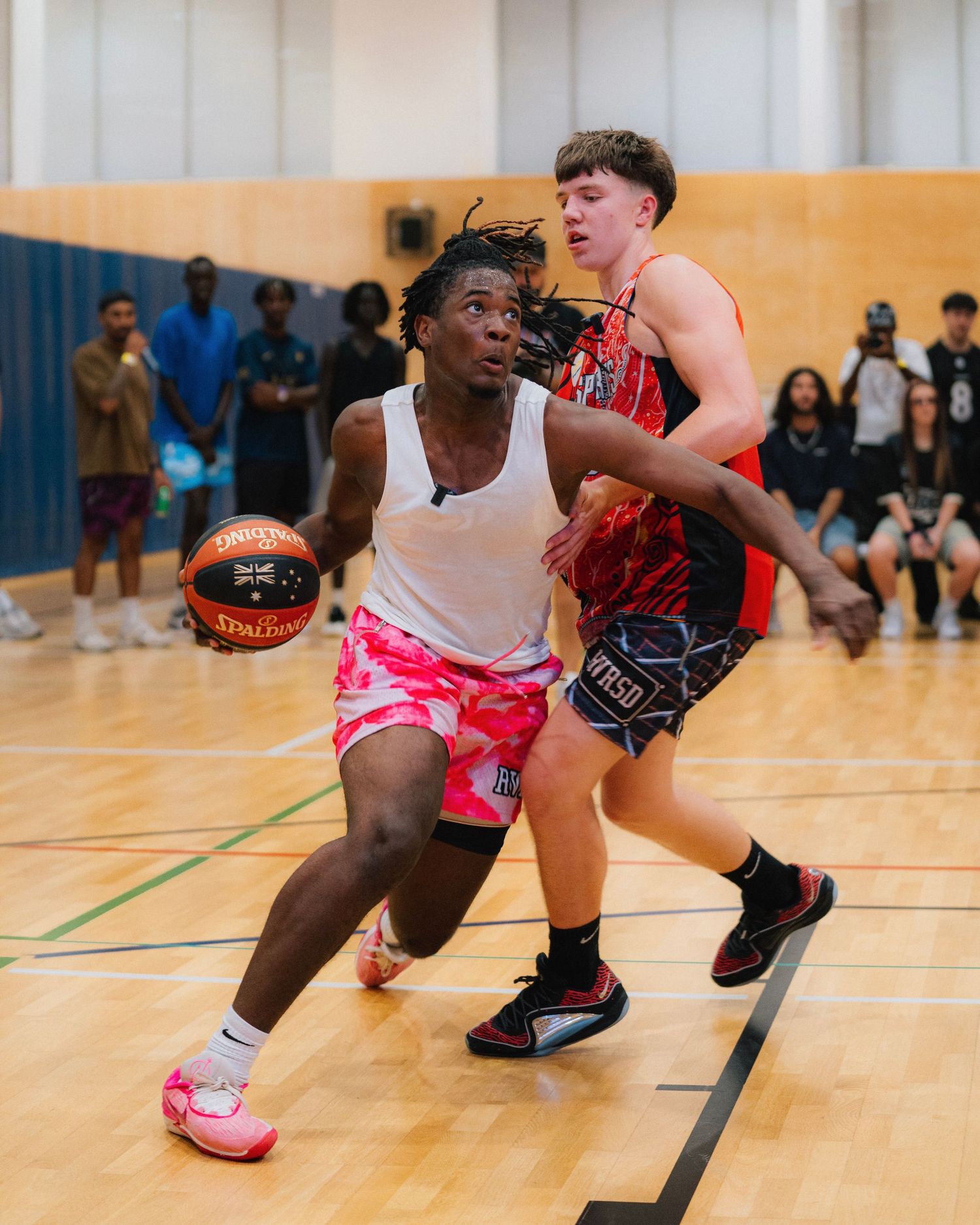 Basketball players compete during an indoor game with one driving past defender.