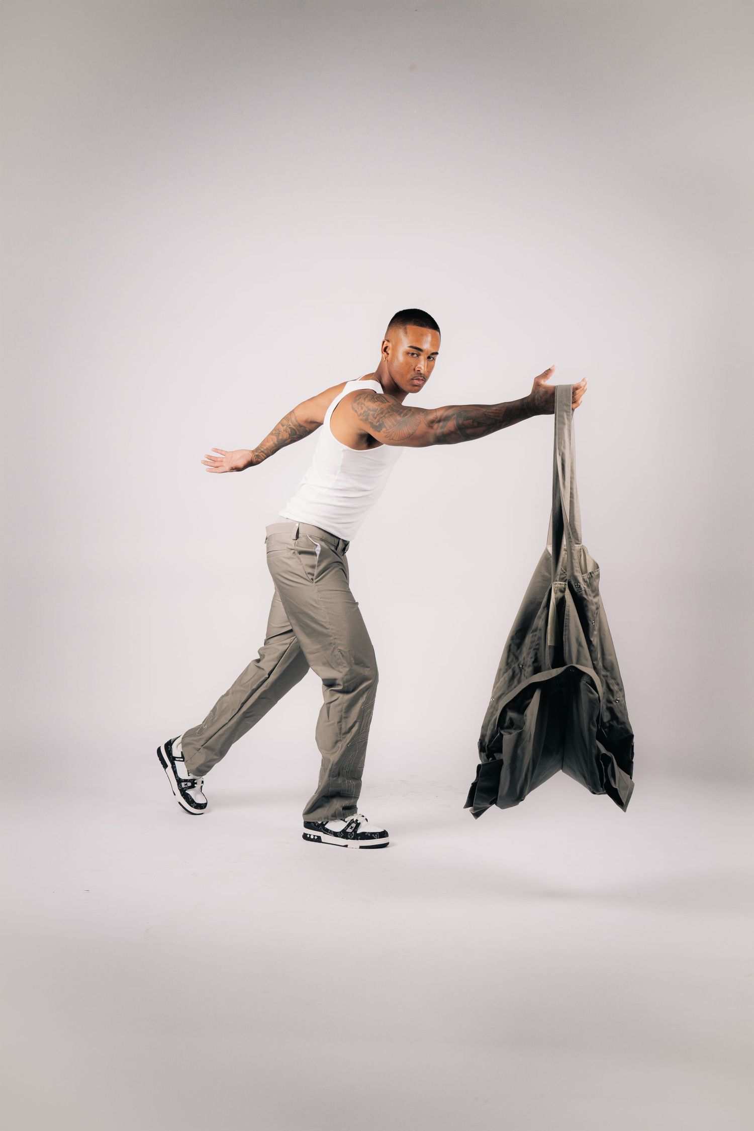 Dynamic fashion pose with model leaning forward holding grey fabric against white background.