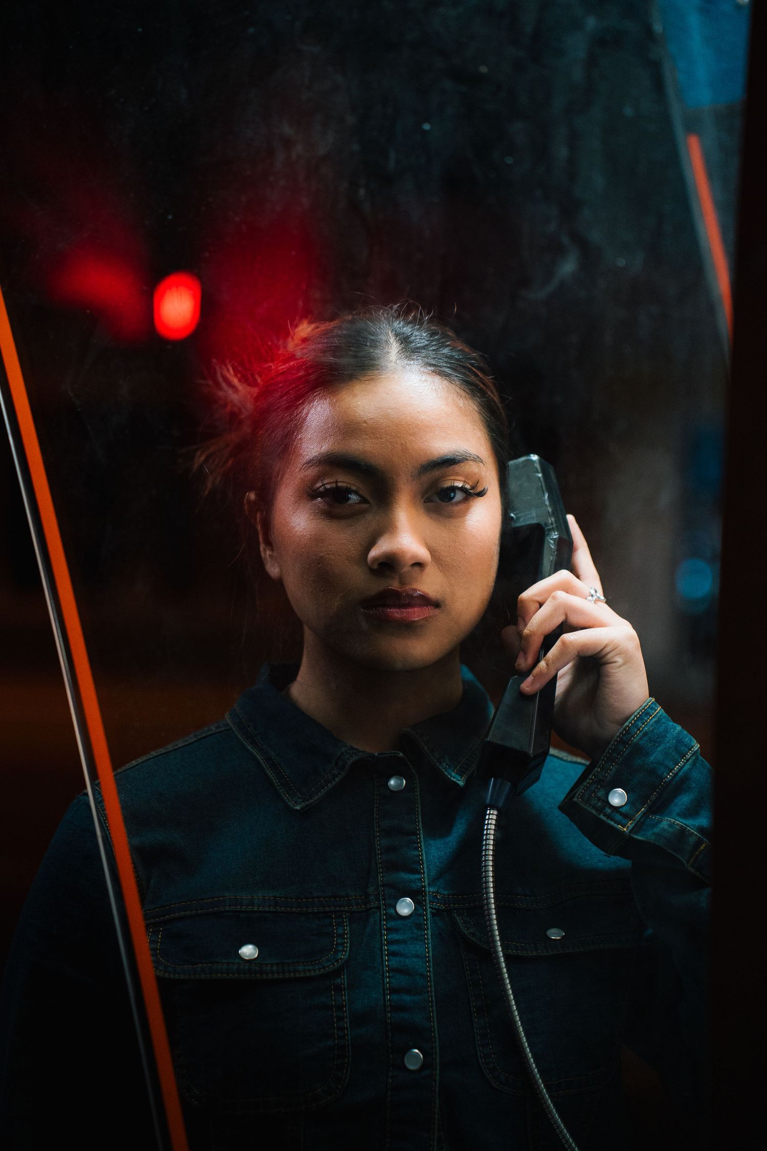 A moody night scene in a phone booth with dramatic red lighting and teal accents against a dark background.