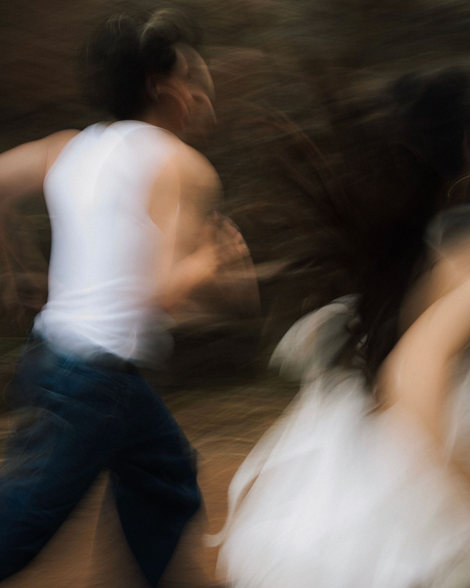 Motion-blurred dancers in white and denim create an artistic swirling effect on a dark background.