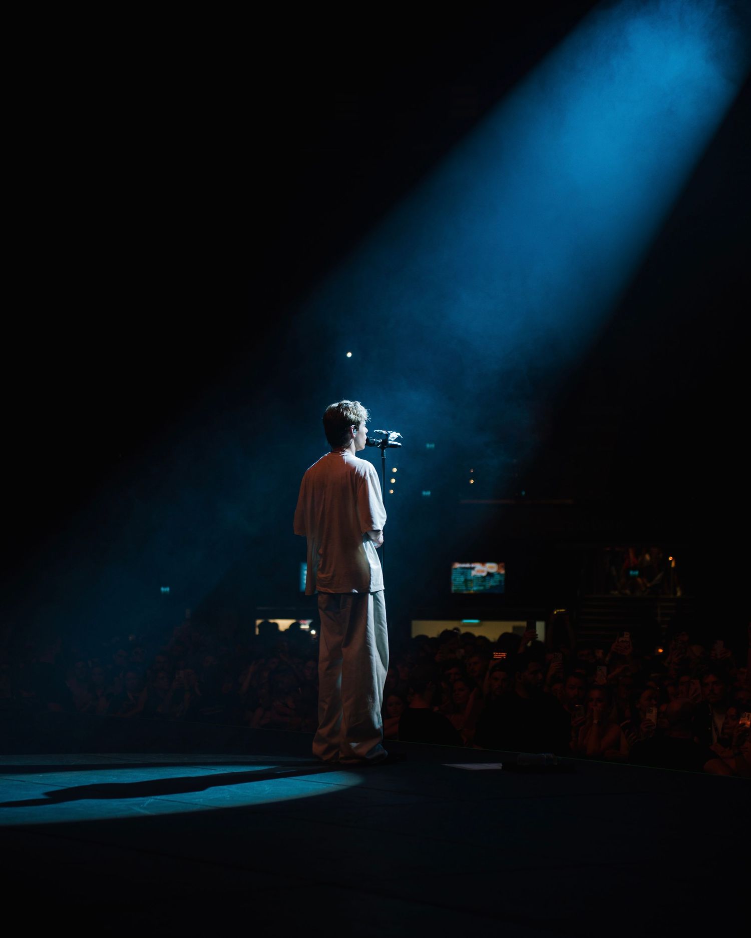 A performer stands in a dramatic blue spotlight on a dark stage during a concert performance.