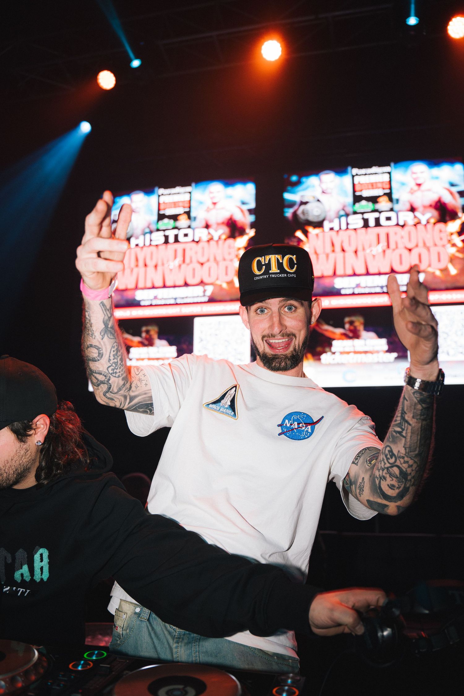 DJ performing at an event with colorful digital displays in the background.