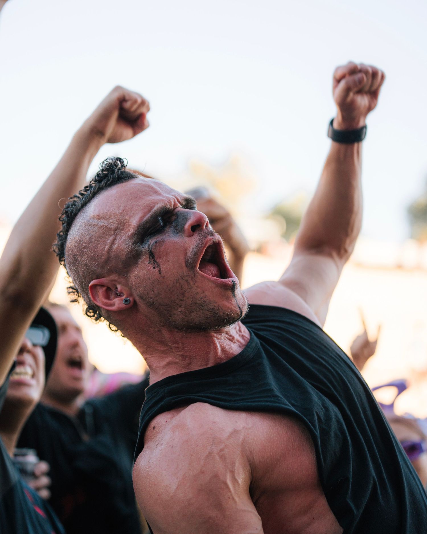 Enthusiastic concert-goer cheering with raised arms during an outdoor music festival.