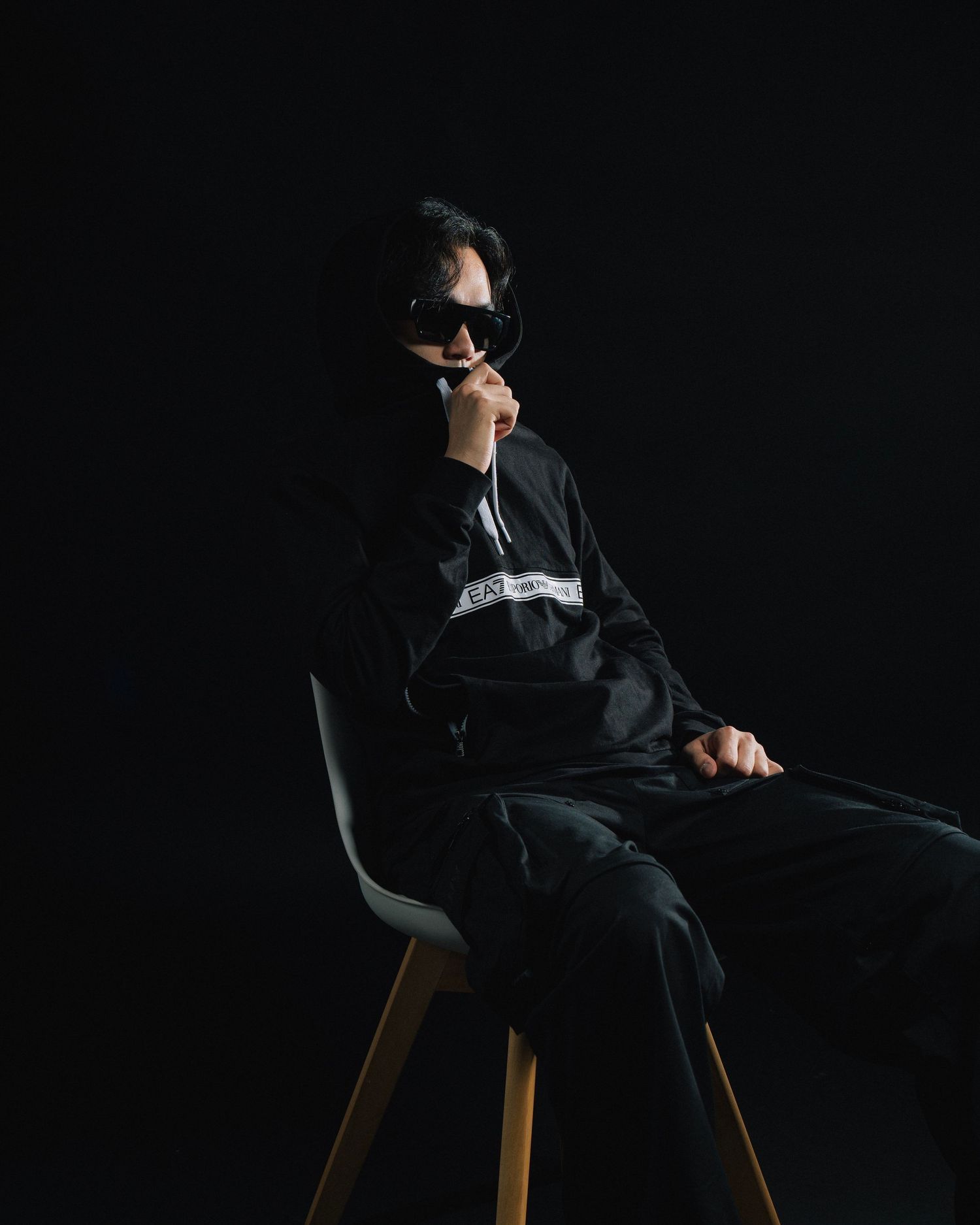 Dramatic portrait of person in black outfit and sunglasses seated on modern chair.
