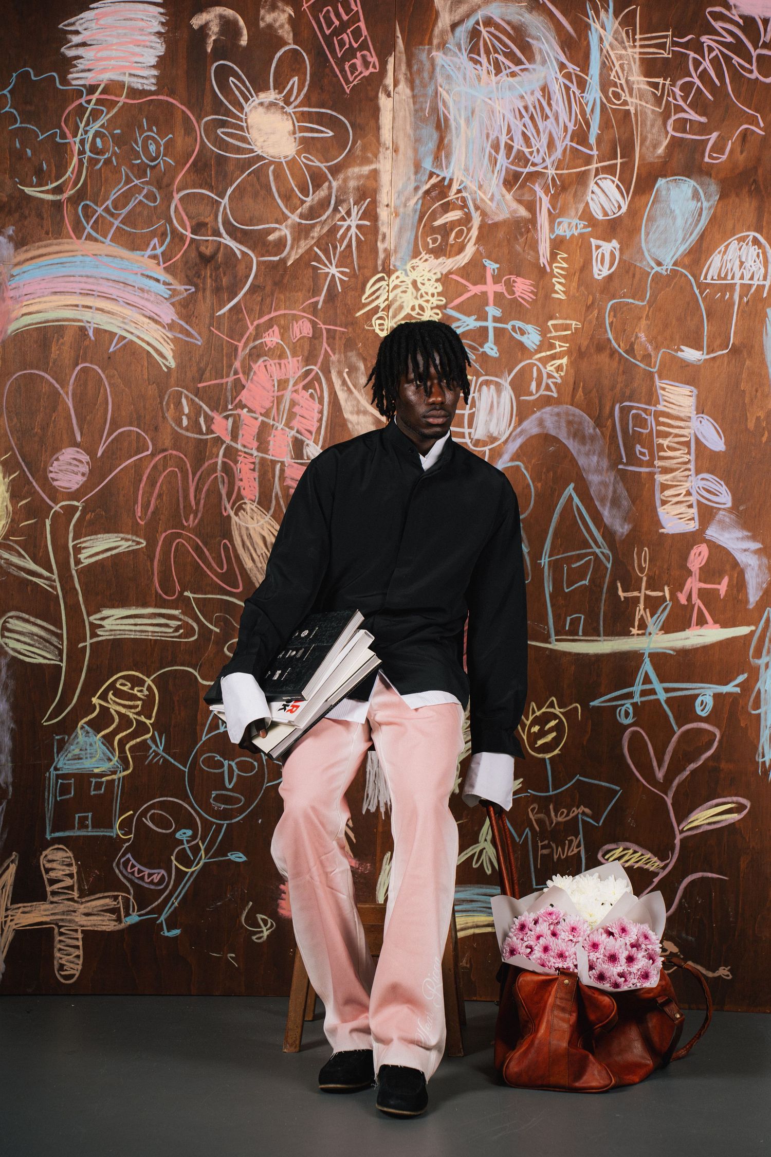 Person in black jacket sits against wall covered in colorful graffiti and doodles.