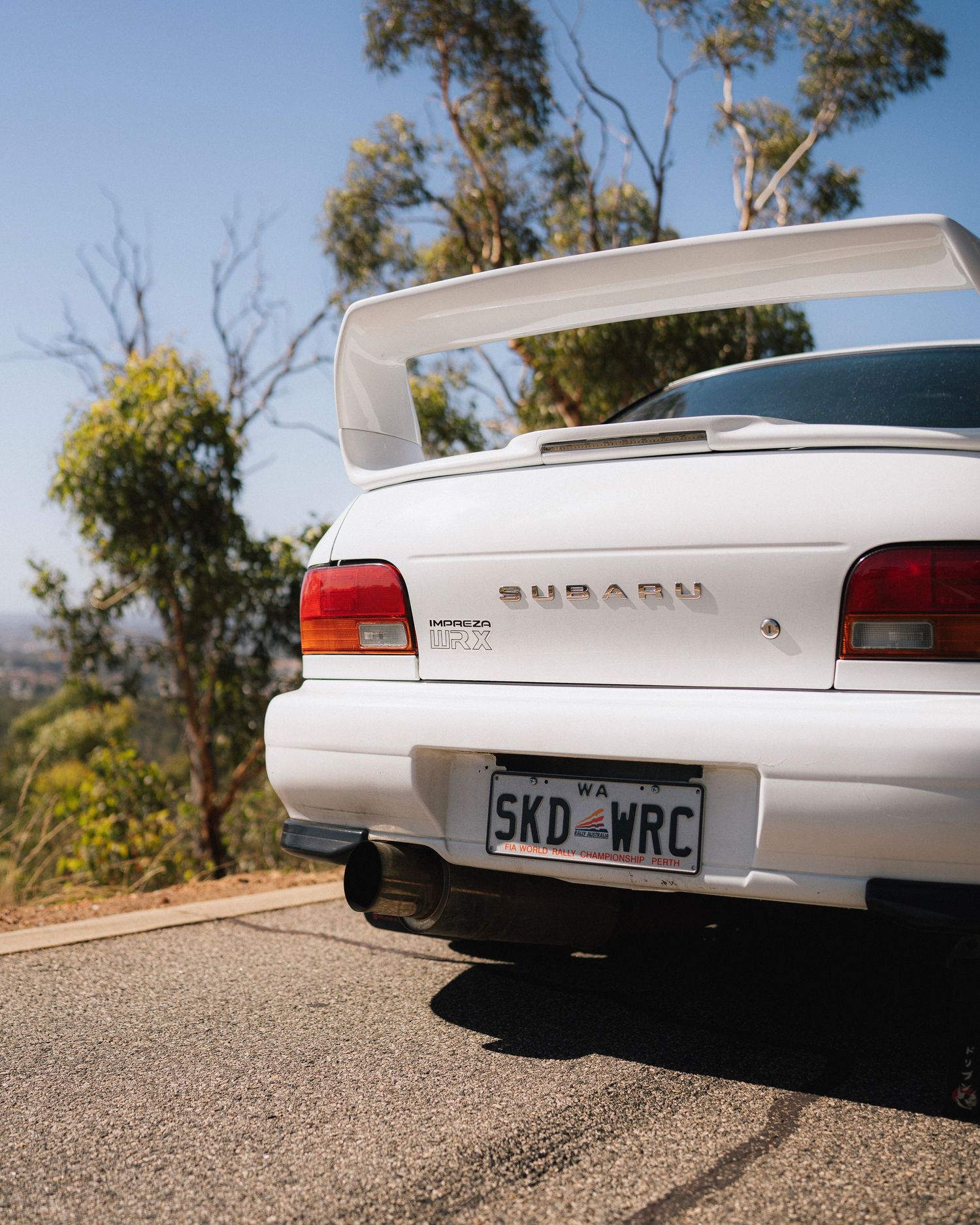White Subaru WRX with large spoiler photographed from rear angle on hilltop.