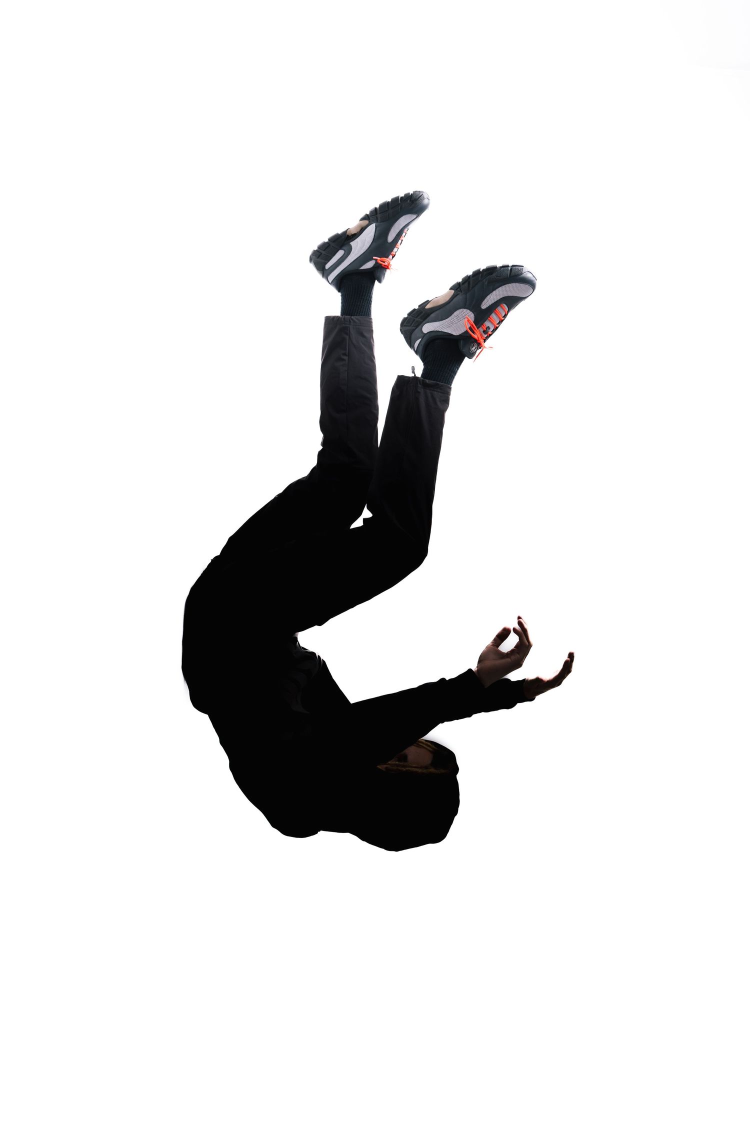 Silhouette of someone falling or jumping while wearing sneakers against a white background.