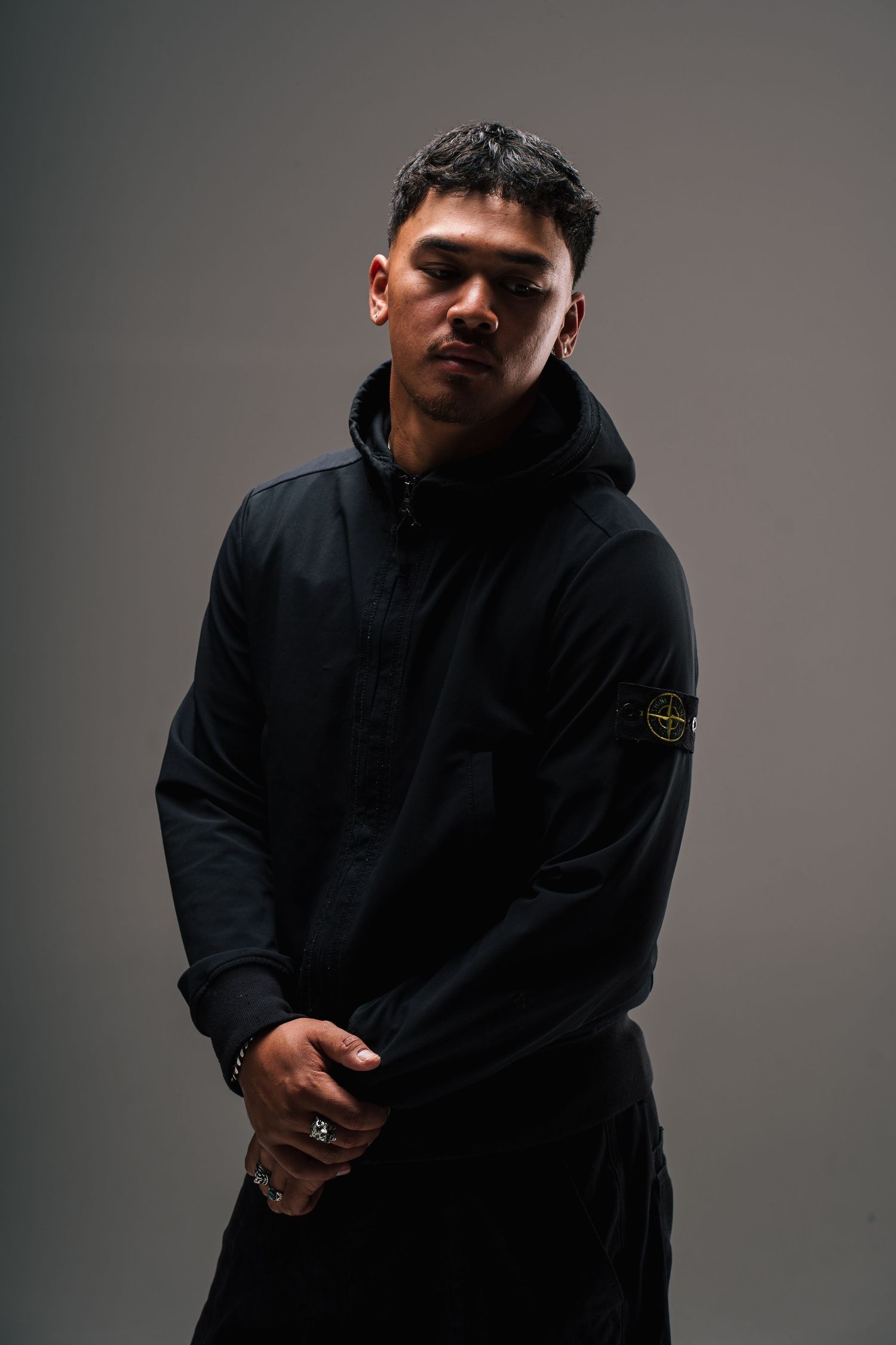 Moody studio portrait of person in dark hoodie with dramatic lighting against gray background.