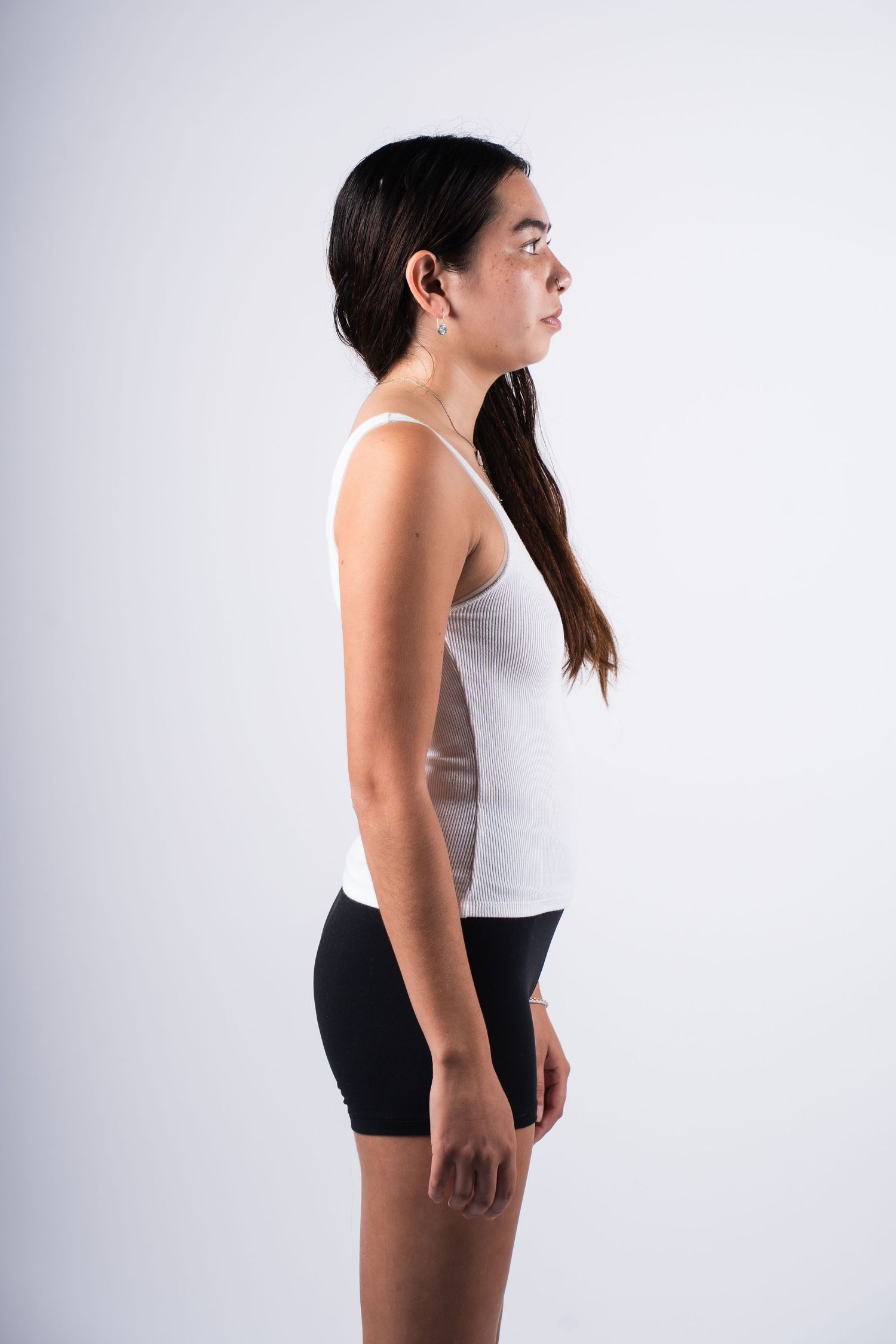 Side profile view of someone wearing a white tank top and black shorts against a light background.