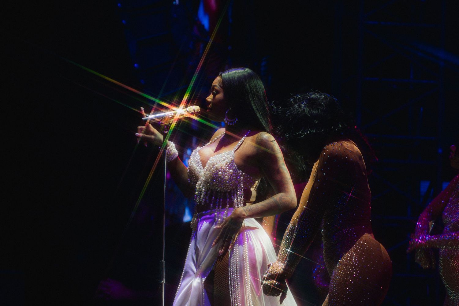 A performer in a sparkly white dress sings on stage with dramatic lighting effects creating a star burst behind them.