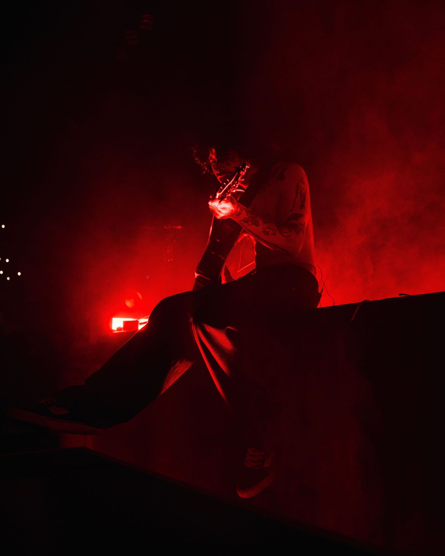 A silhouetted figure sits illuminated by intense red lighting and smoke effects during a moody nighttime scene.