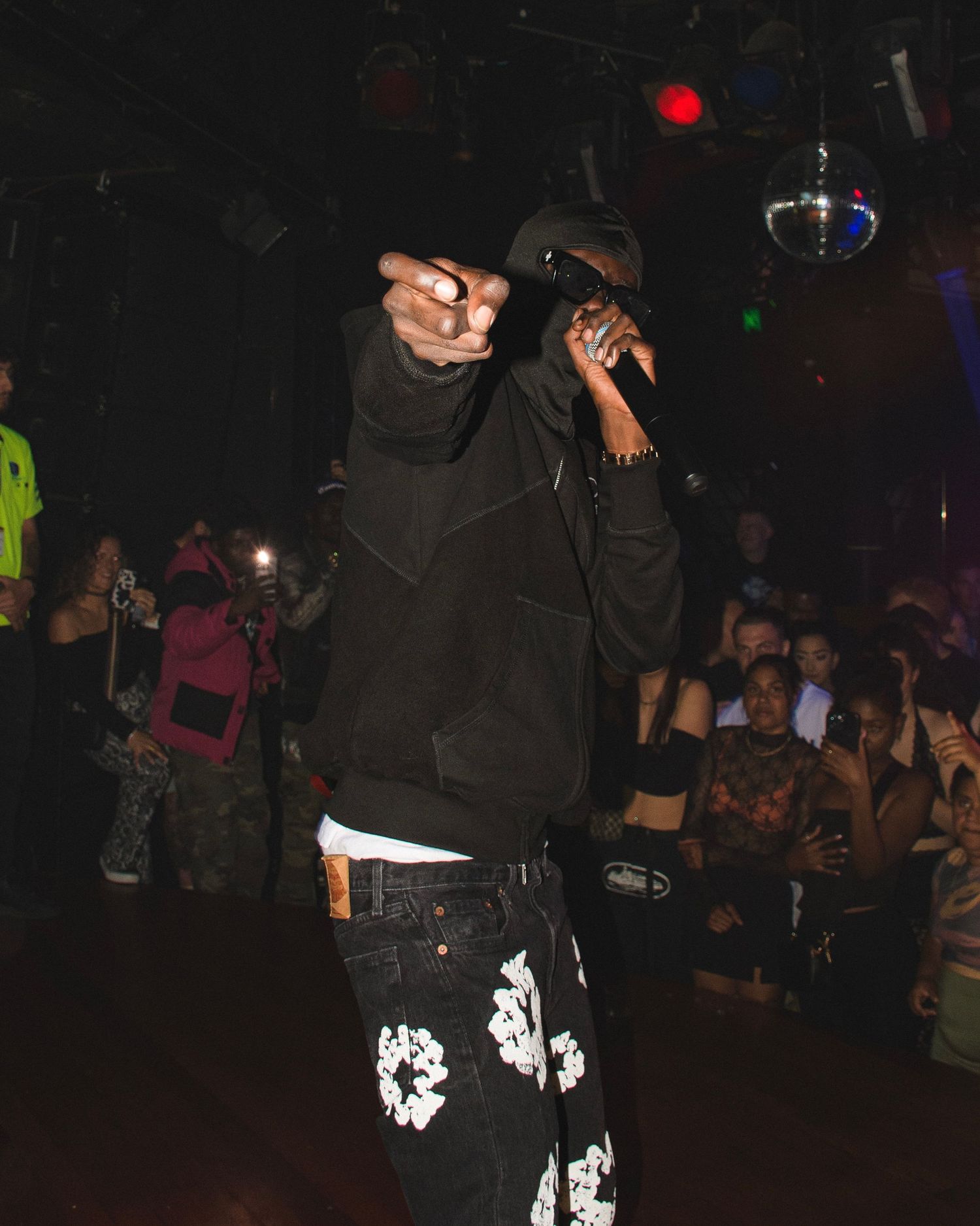 Performer in black hoodie and patterned pants performing at nightclub venue.