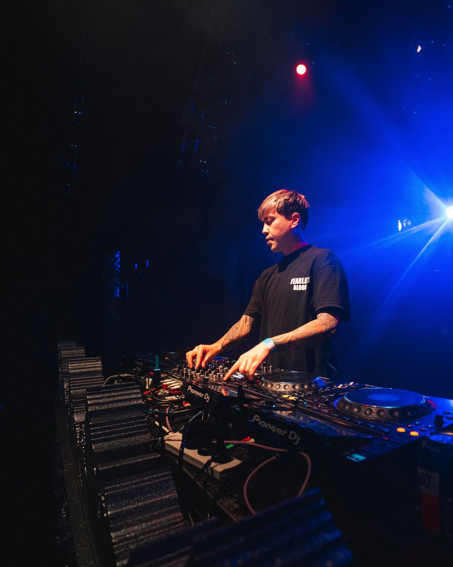 DJ performing on stage with professional equipment under dramatic blue lighting at a nightclub.
