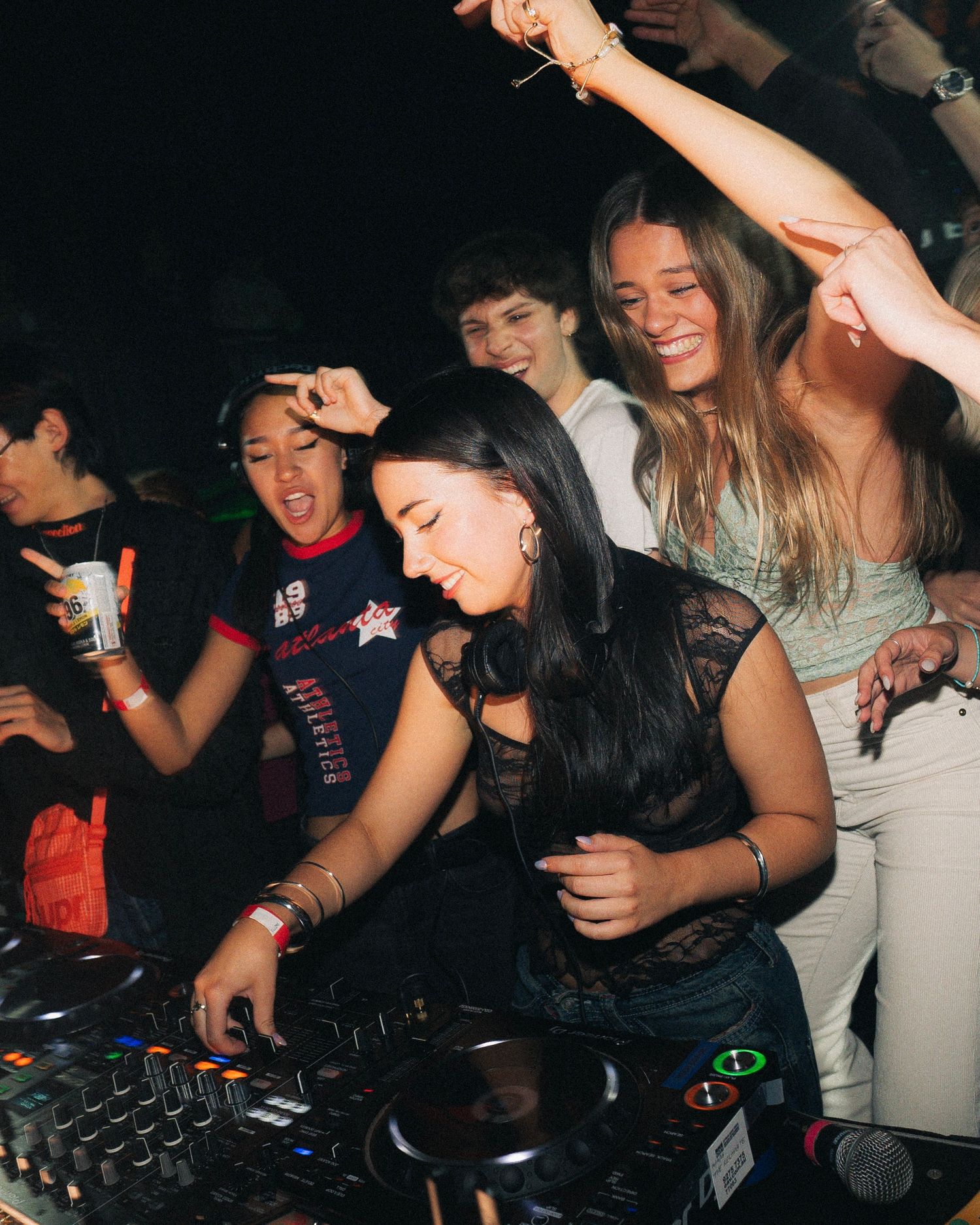 Energetic crowd dancing and cheering around DJ equipment at a nightclub party.