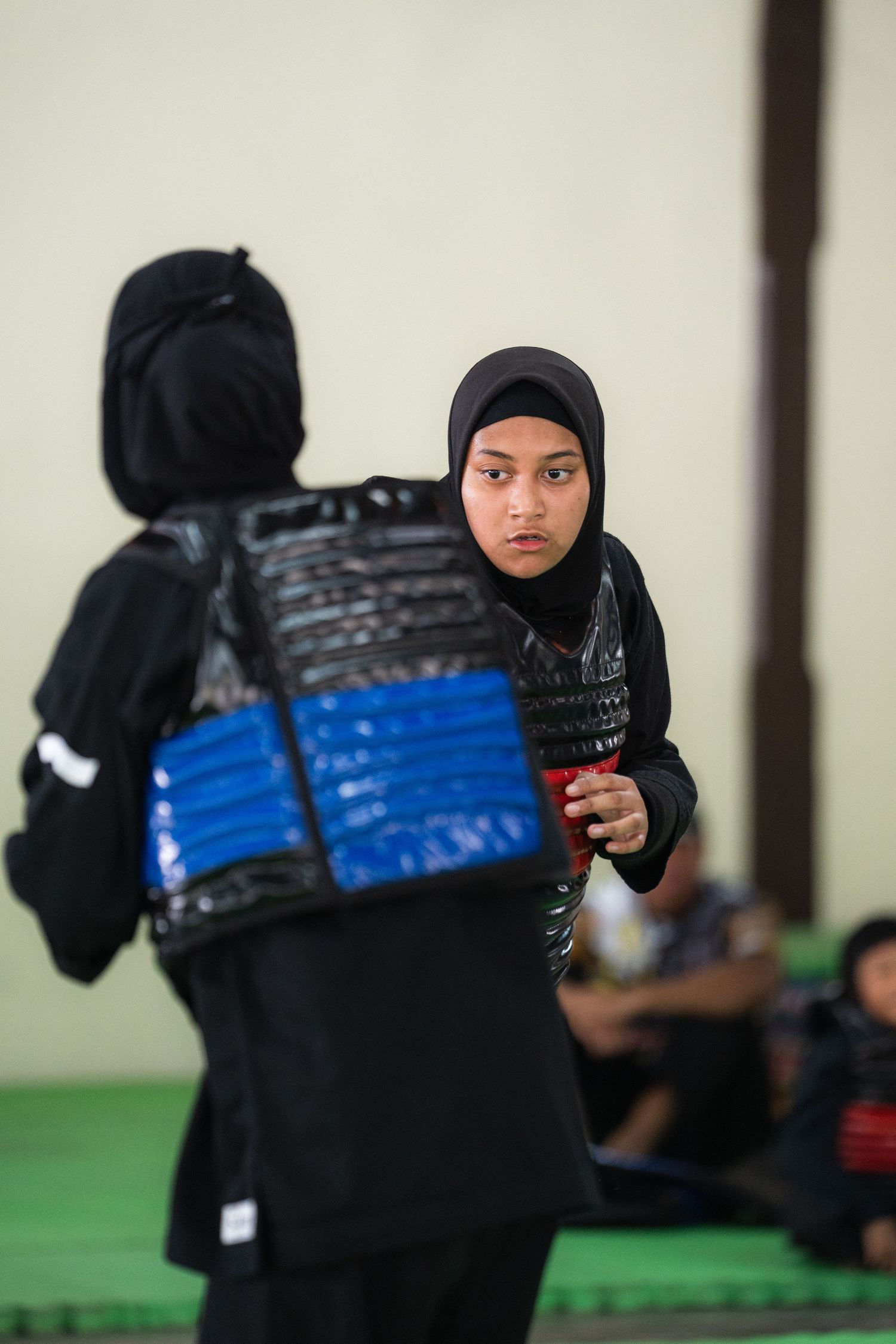 Two athletes in hijabs face off during sports training in an indoor setting.