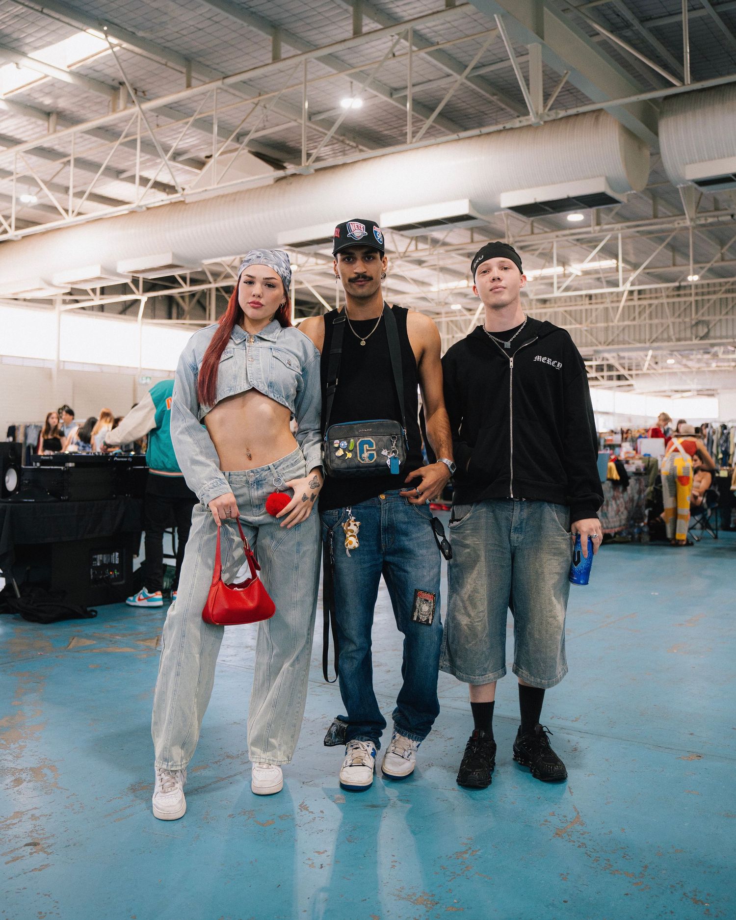 Three people in casual streetwear posing together in a warehouse setting.