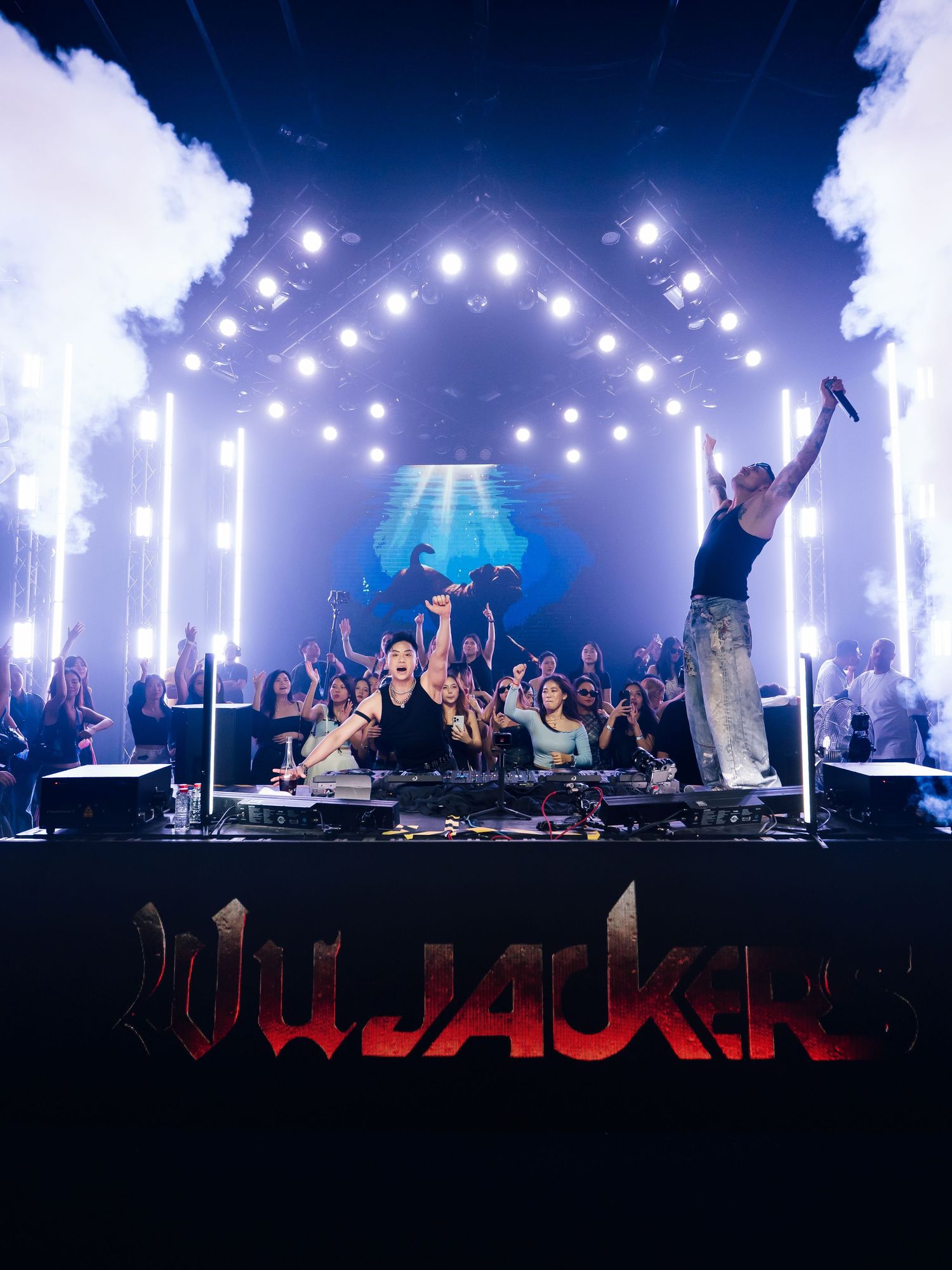 Concert crowd silhouetted against dramatic stage lighting with glowing white spotlights and blue illumination during performance.
