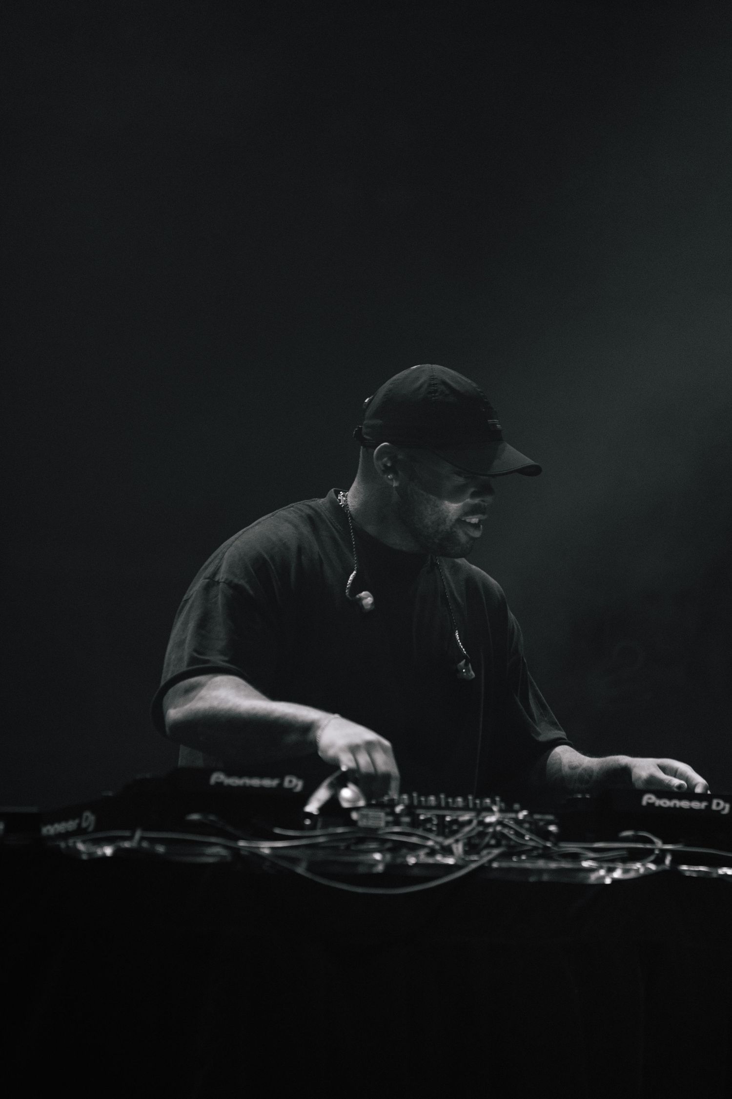 DJ performing at dark venue with Pioneer equipment in atmospheric black and white photo.