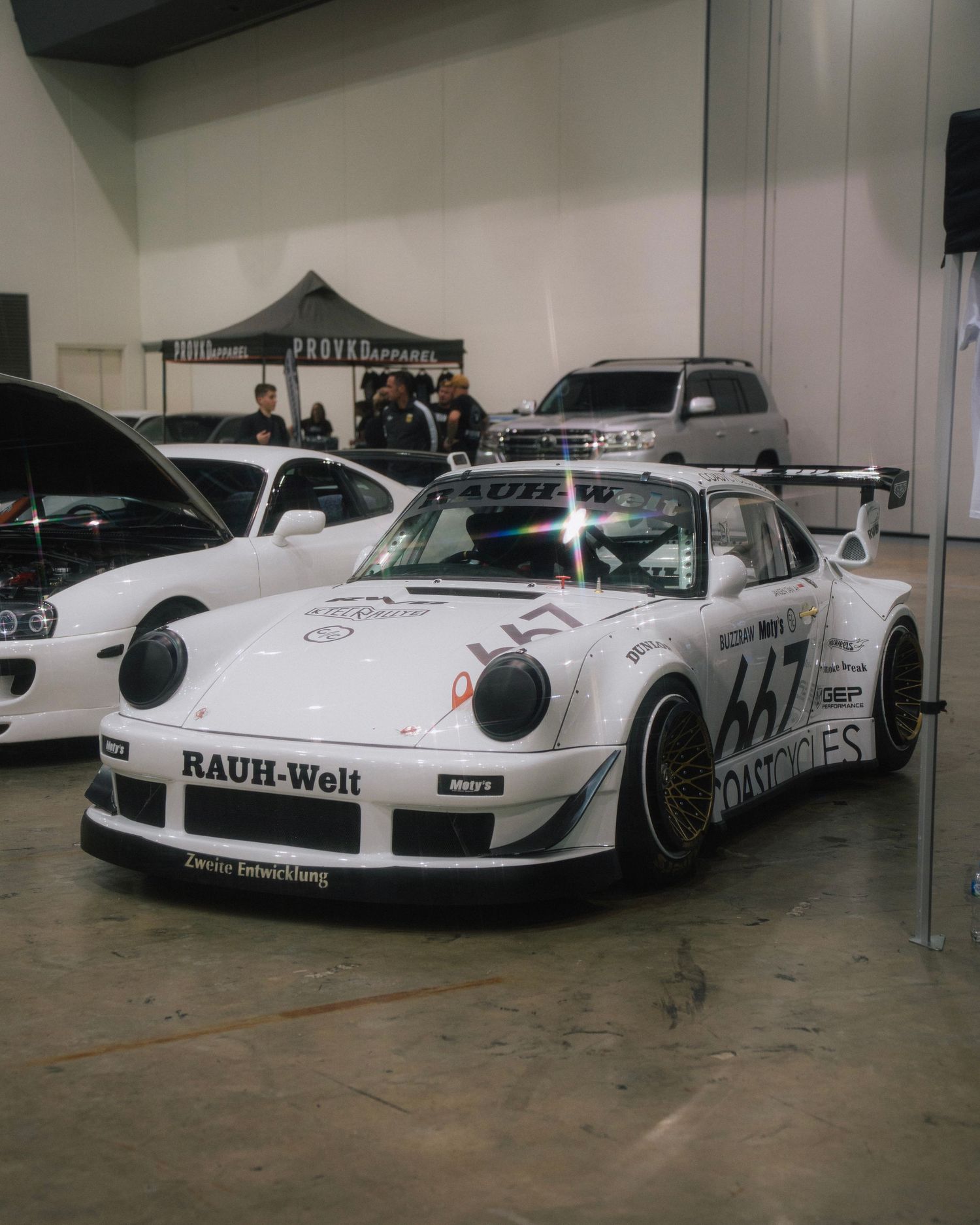 White Porsche 911 RWB race car with wide body kit and racing livery displayed at indoor show.
