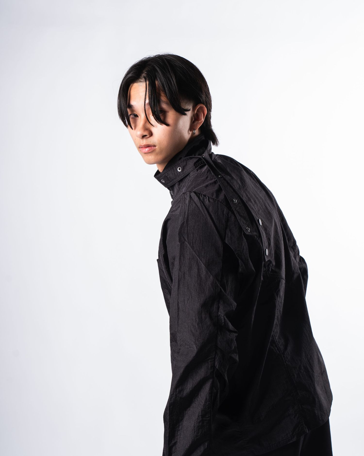 Person in black jacket with long hair posing against white background.