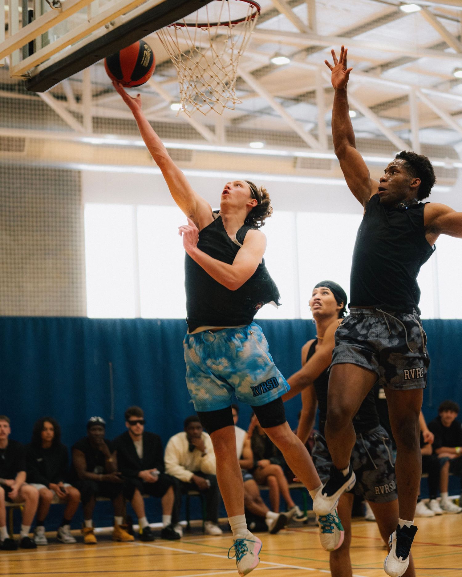 Basketball players compete in an indoor gym, with one attempting a layup while another defends.