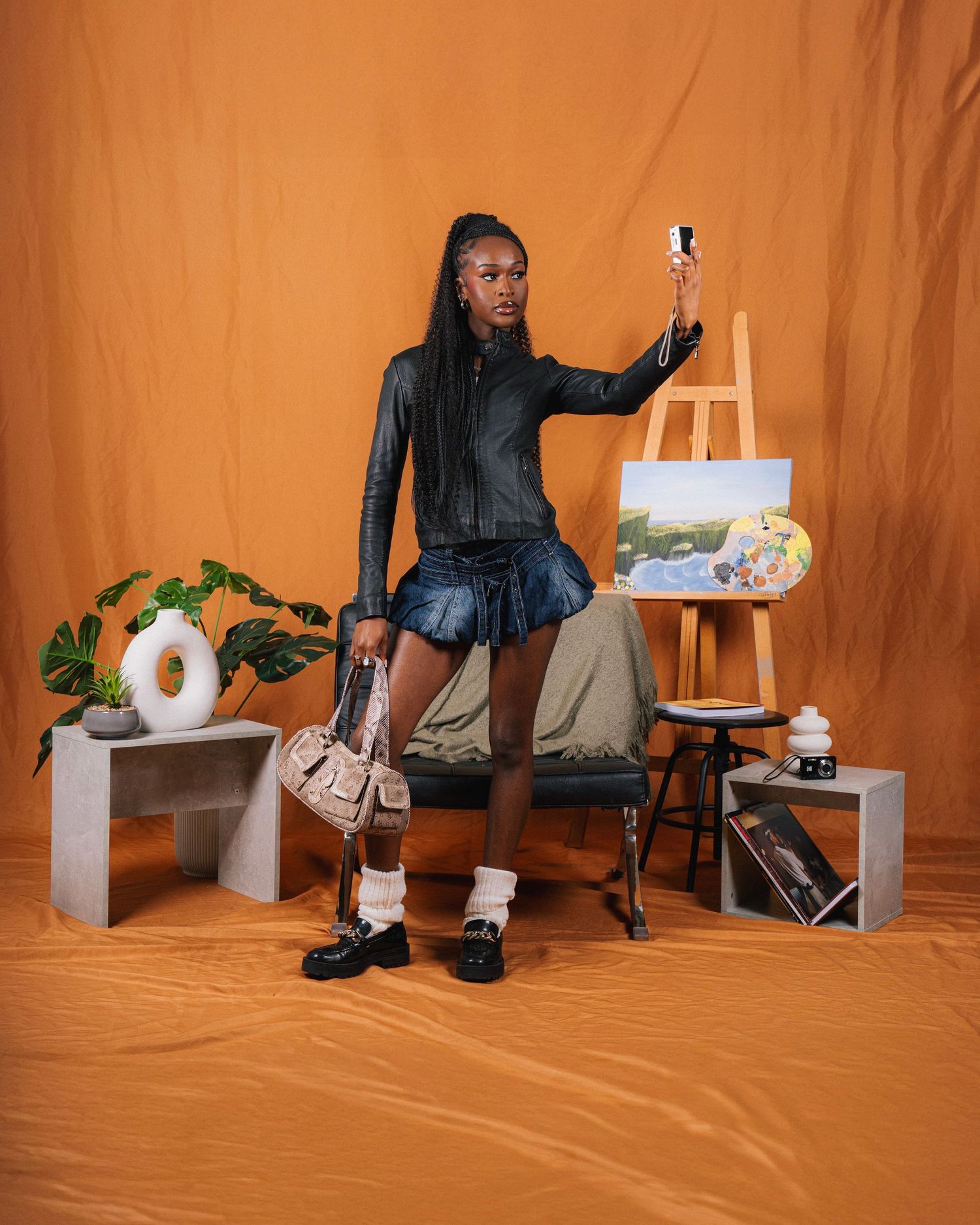 Person seated on wooden stool against orange backdrop holding paper towel and bottle in artistic photoshoot sequence.