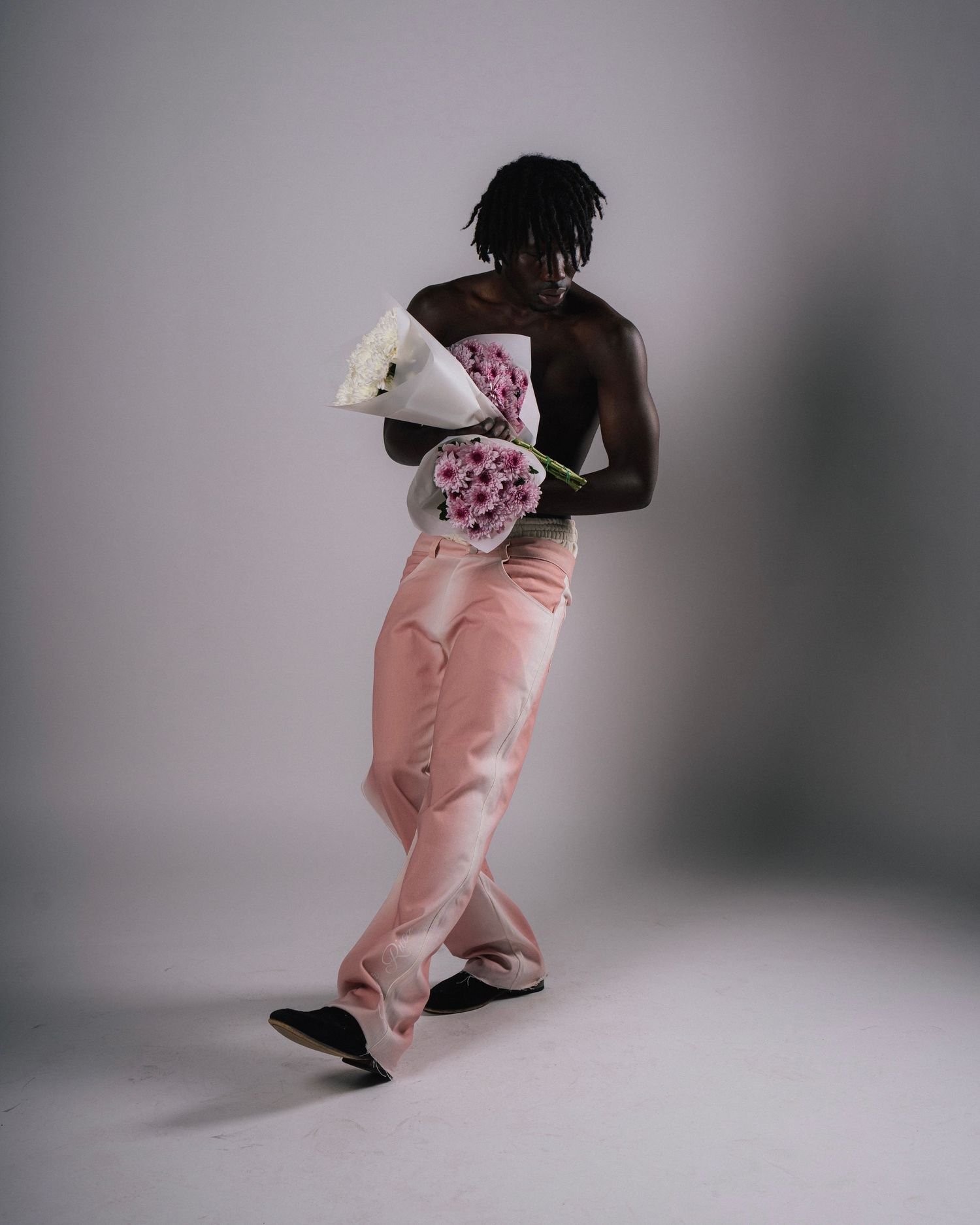 Figure in pink pants holding bouquet of flowers in studio setting.