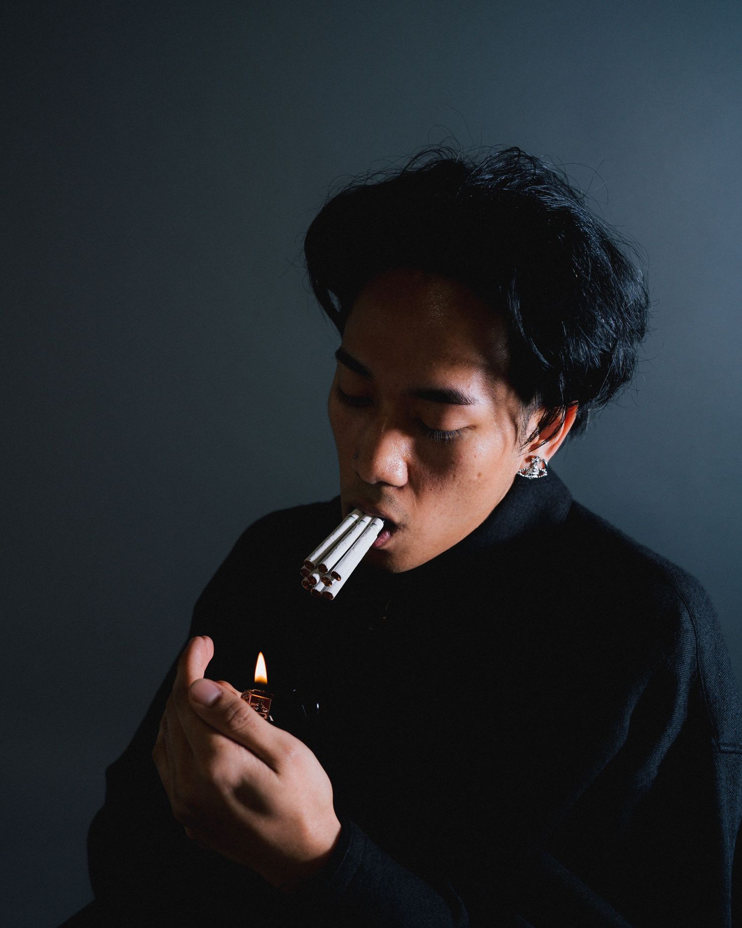 Person in black clothing lighting multiple cigarettes in dramatic studio lighting.