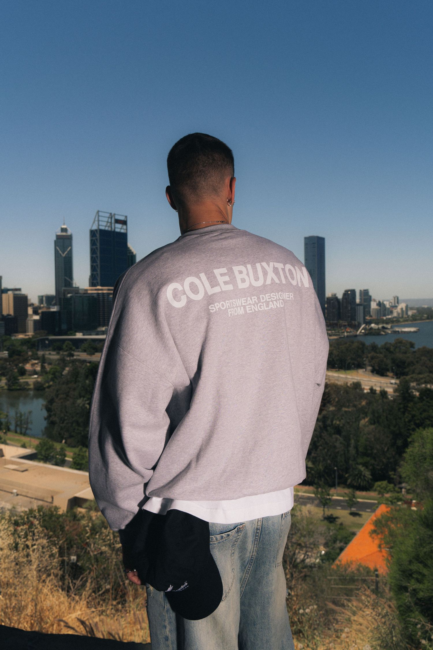 Person wearing Cole Buxton sweatshirt overlooking city skyline.
