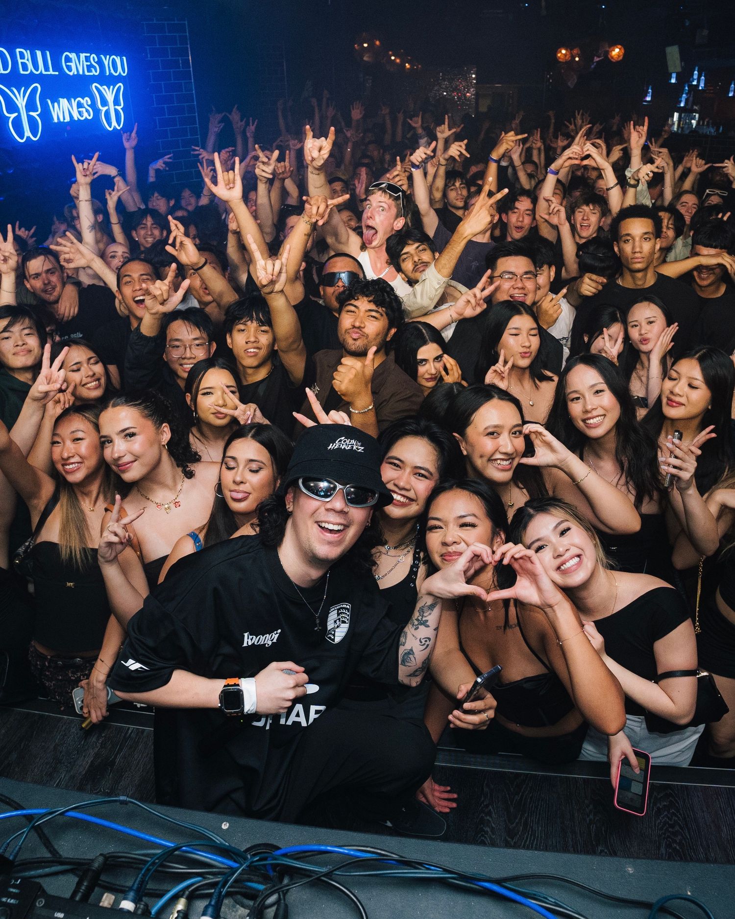 Large crowd of excited fans at a concert venue with neon lighting.