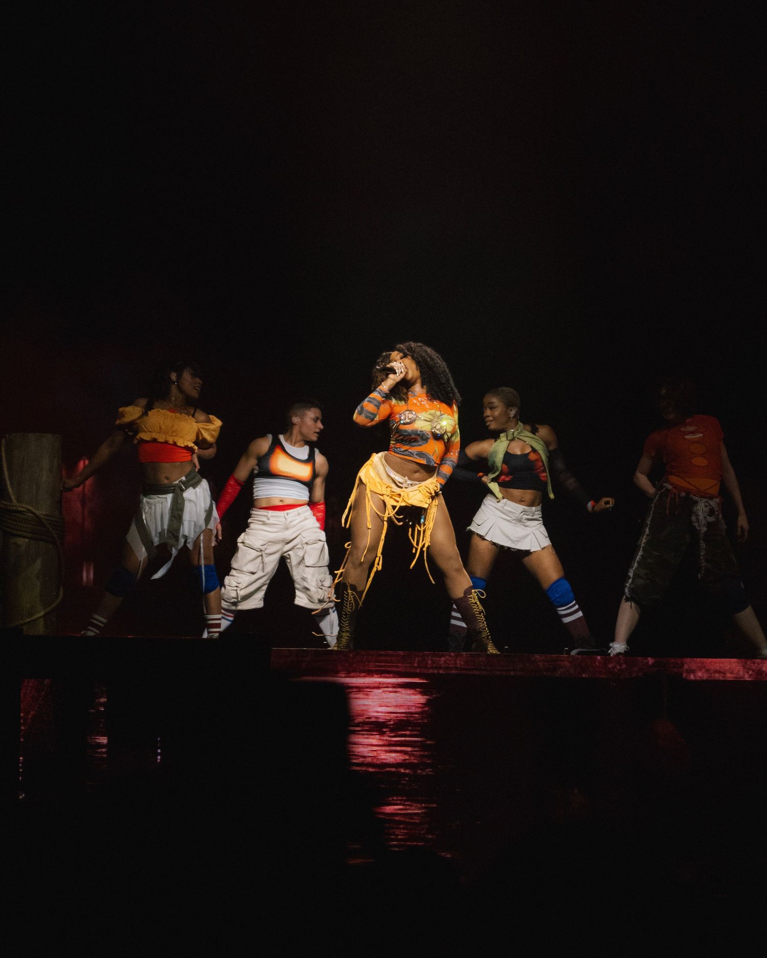 A theatrical performance on stage with dancers in colorful costumes performing a hip-hop routine under dramatic lighting.