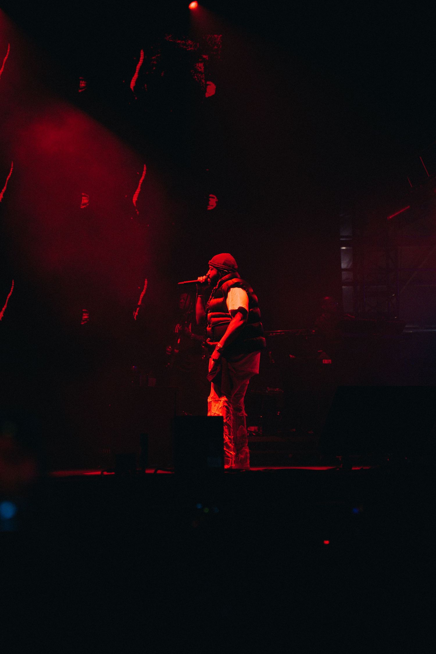 A performer silhouetted against red stage lighting stands with a microphone during a concert performance.