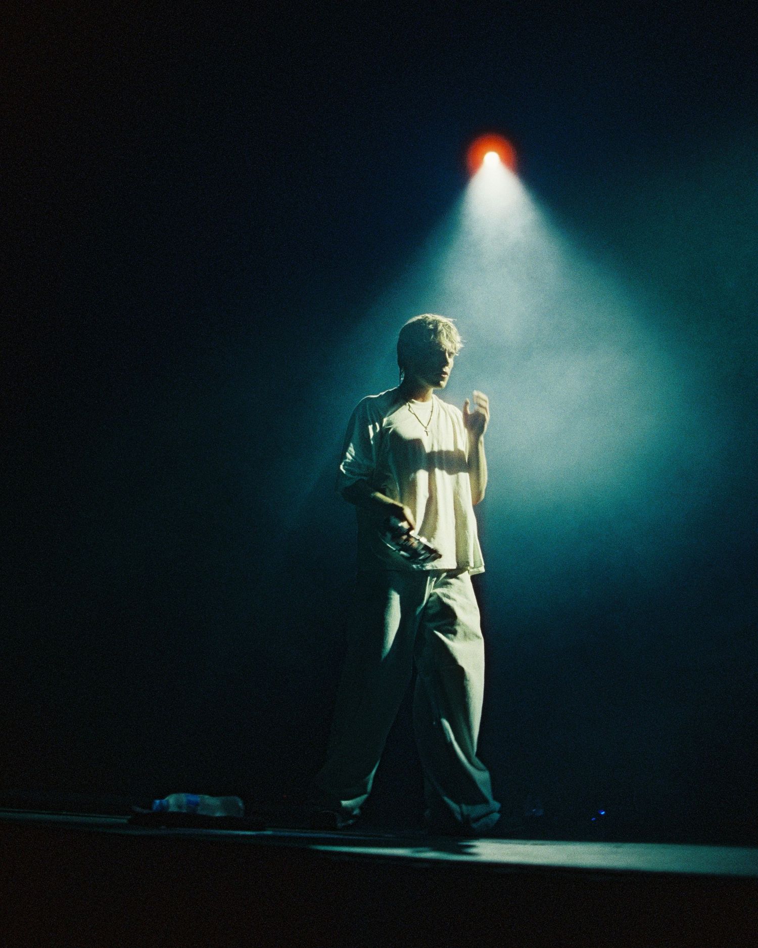 A performer stands in silhouette under a dramatic spotlight beam on a dark stage creating an atmospheric scene.