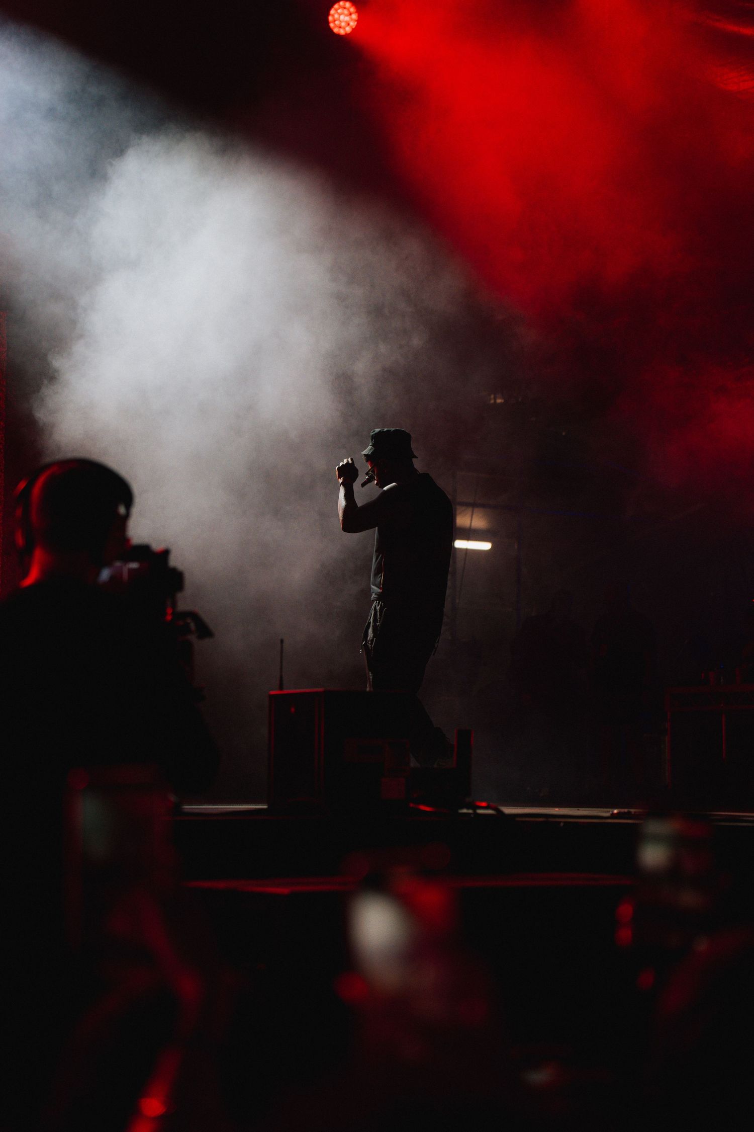 A silhouetted performer stands on stage amid dramatic red and white smoke effects at a concert venue.