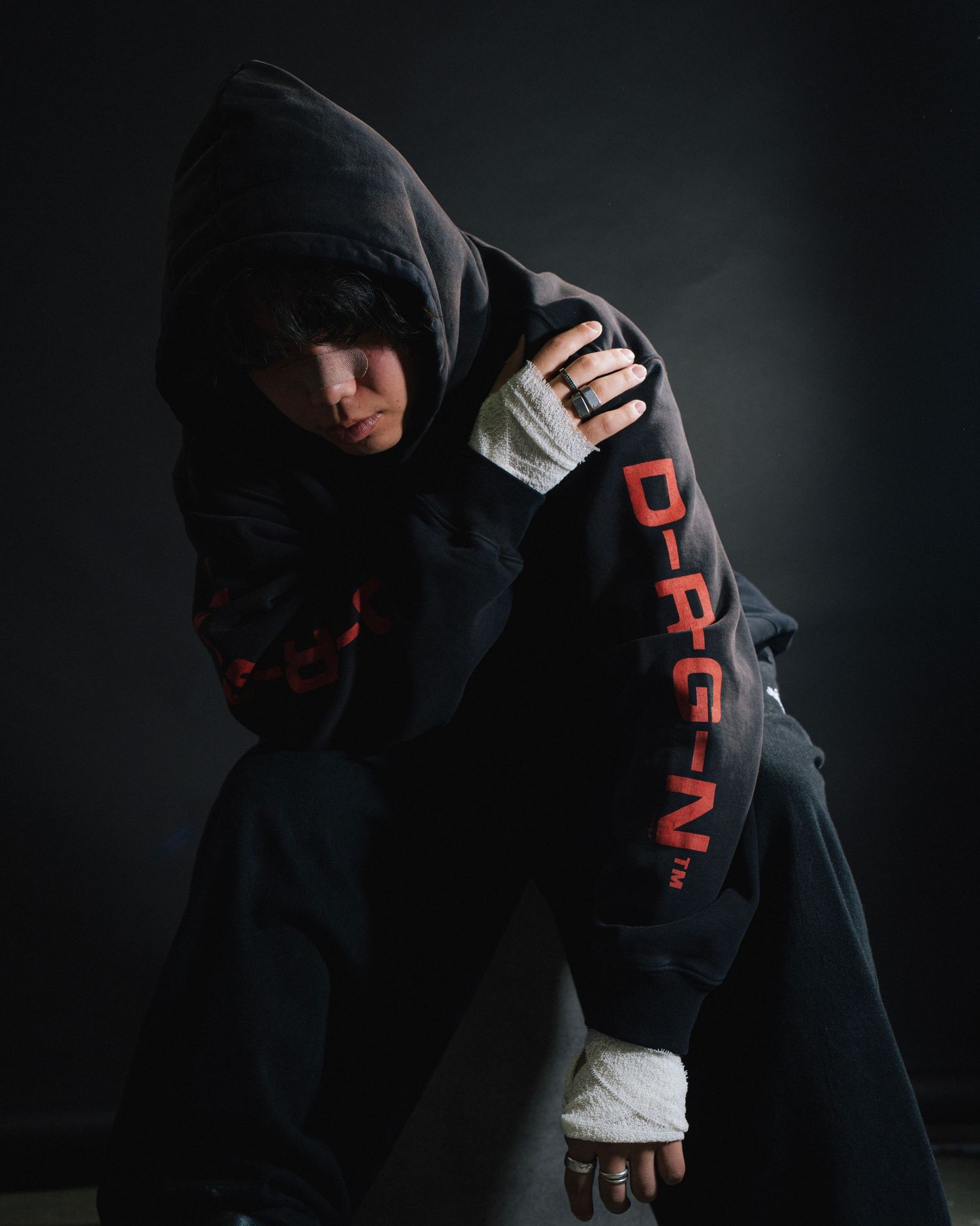 Dramatic portrait of person in black Dragon hoodie against dark background.