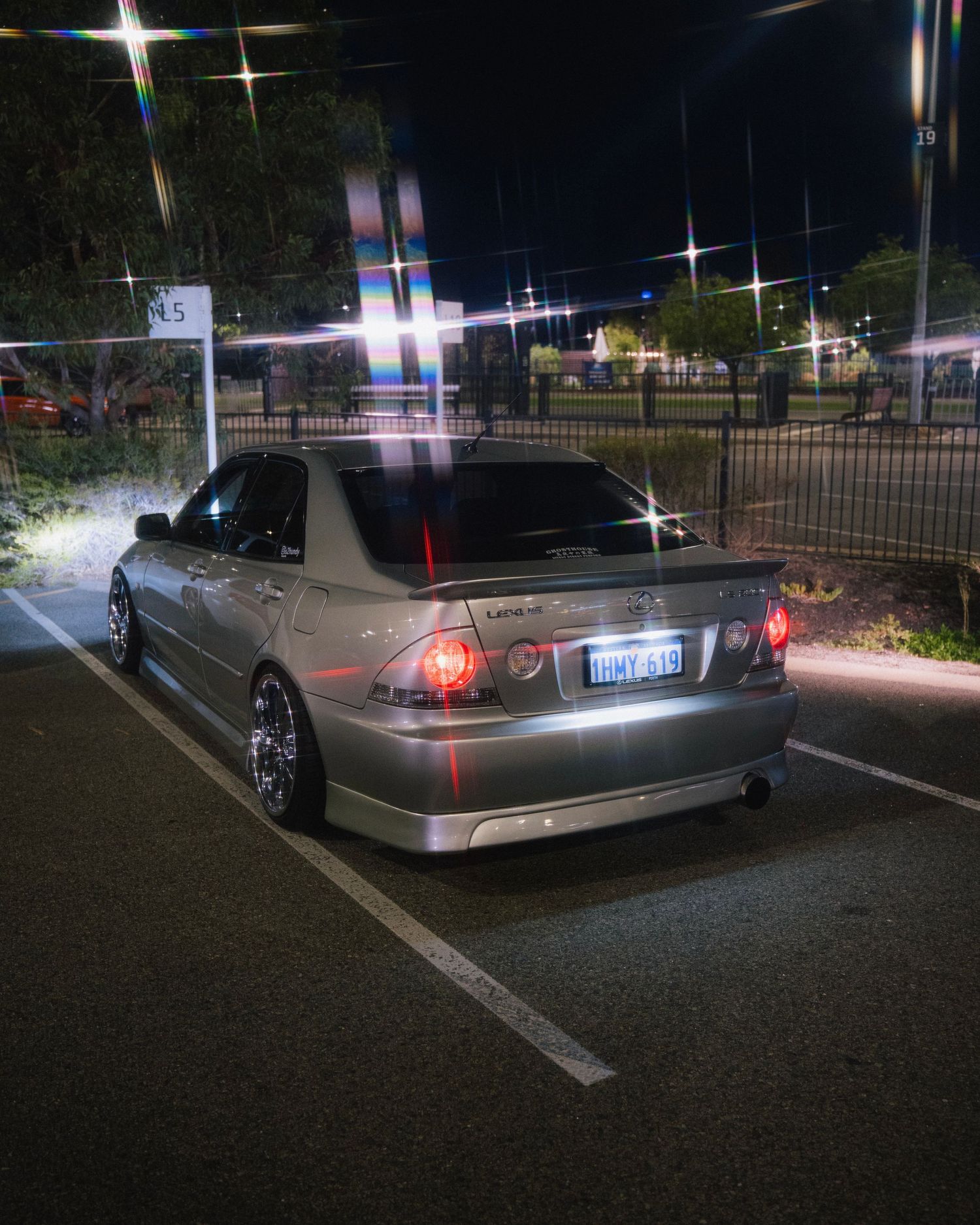 Modified silver Lexus IS300 parked at night with custom wheels and lighting effects.