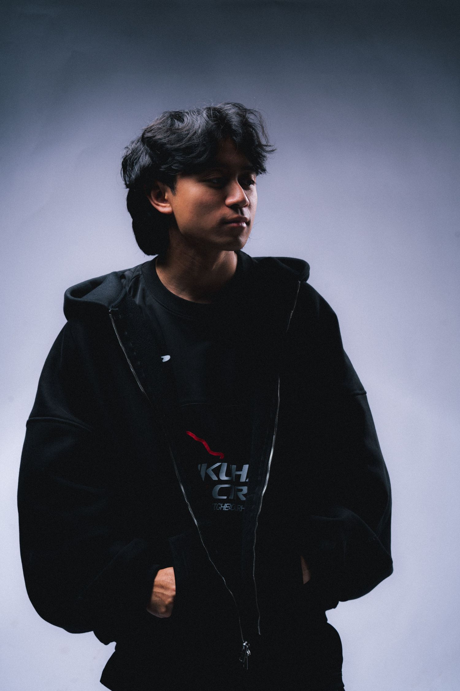 A youth wearing a black hoodie gazes to the side in moody lighting.
