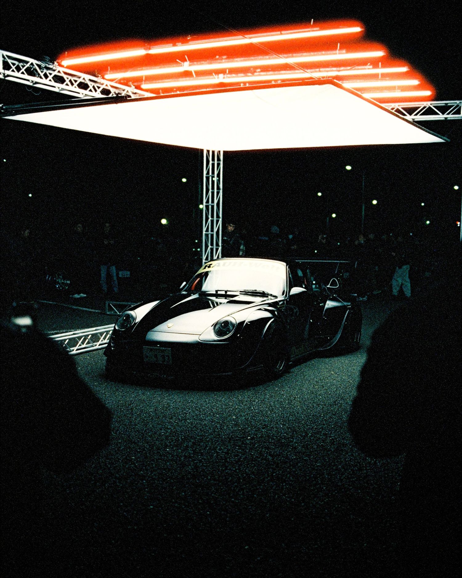 Sports car displayed under illuminated white canopy with red neon lighting.